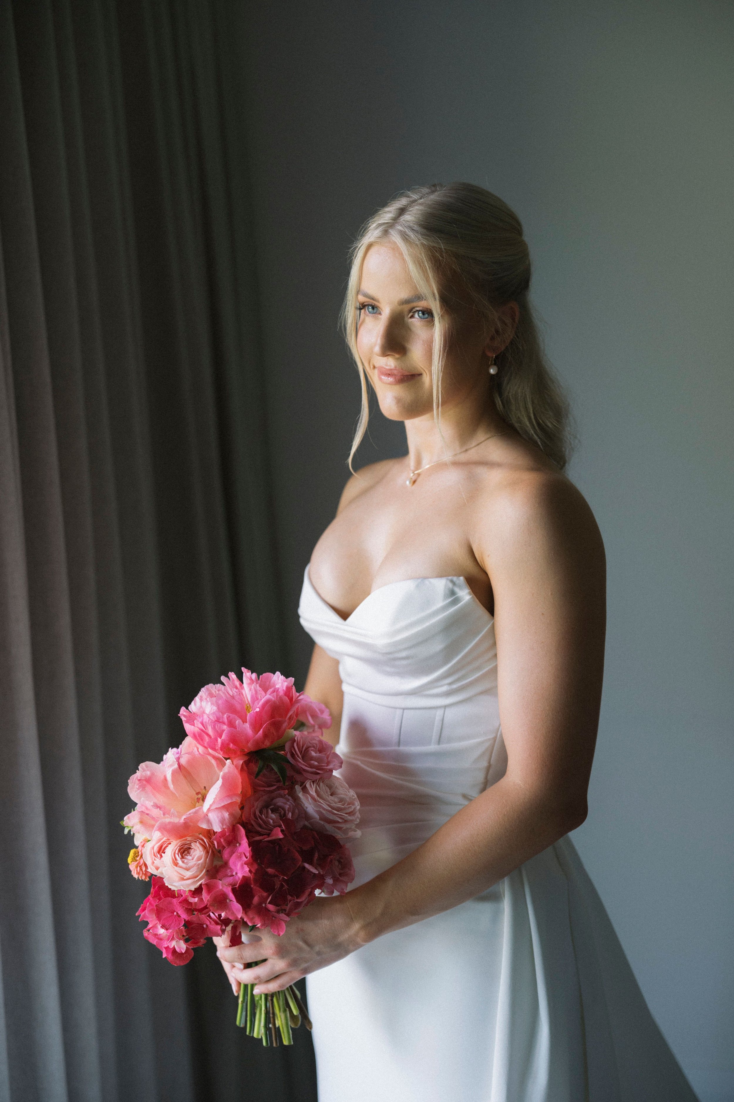 Bride in a white wedding dress holding a bouquet of pink flowers.