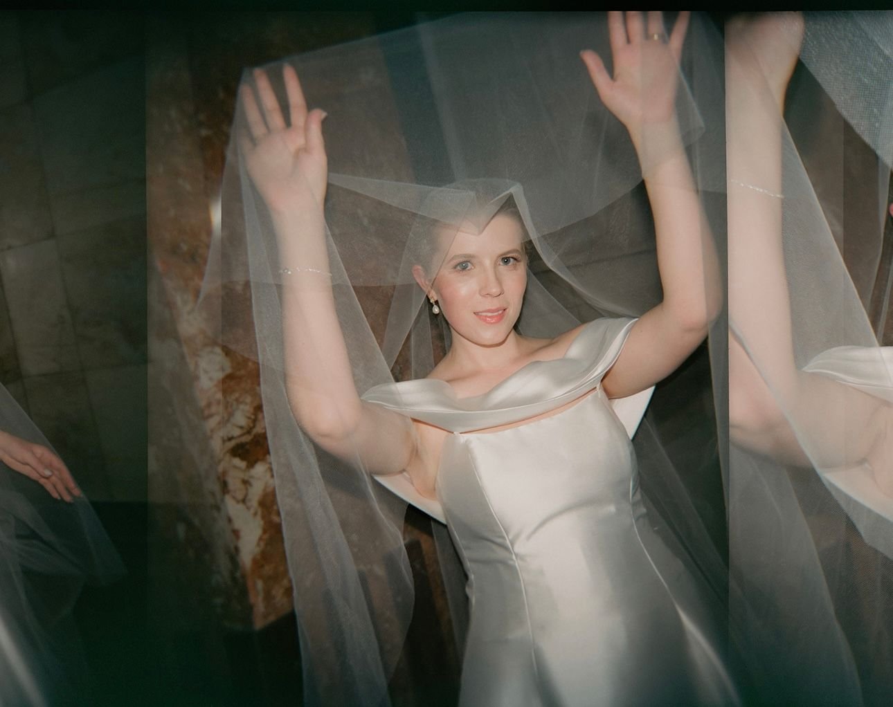 Bride in white wedding dress with veil raised, smiling.