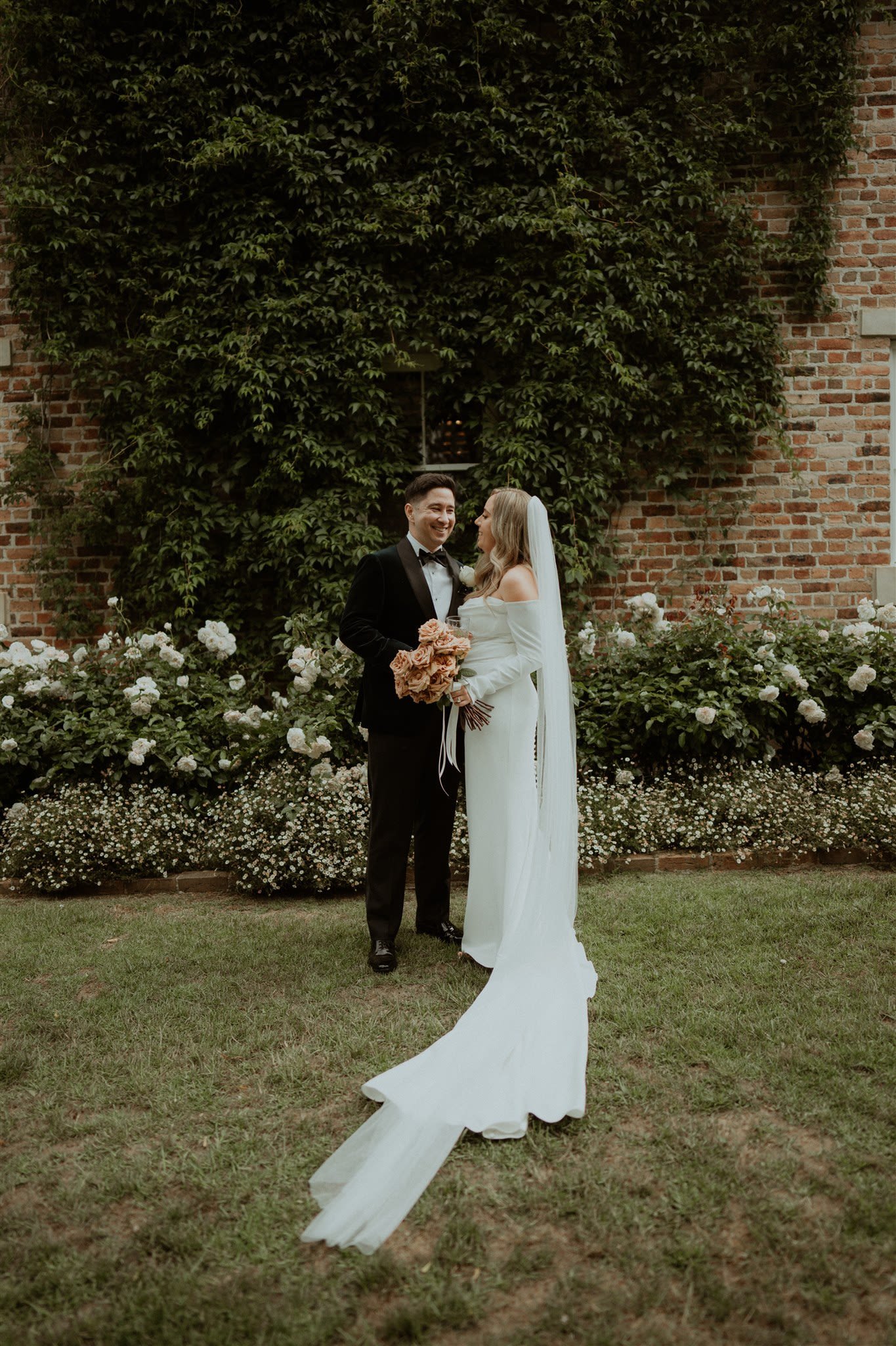 Wedding couple smiling in a garden with a brick wall and green foliage background