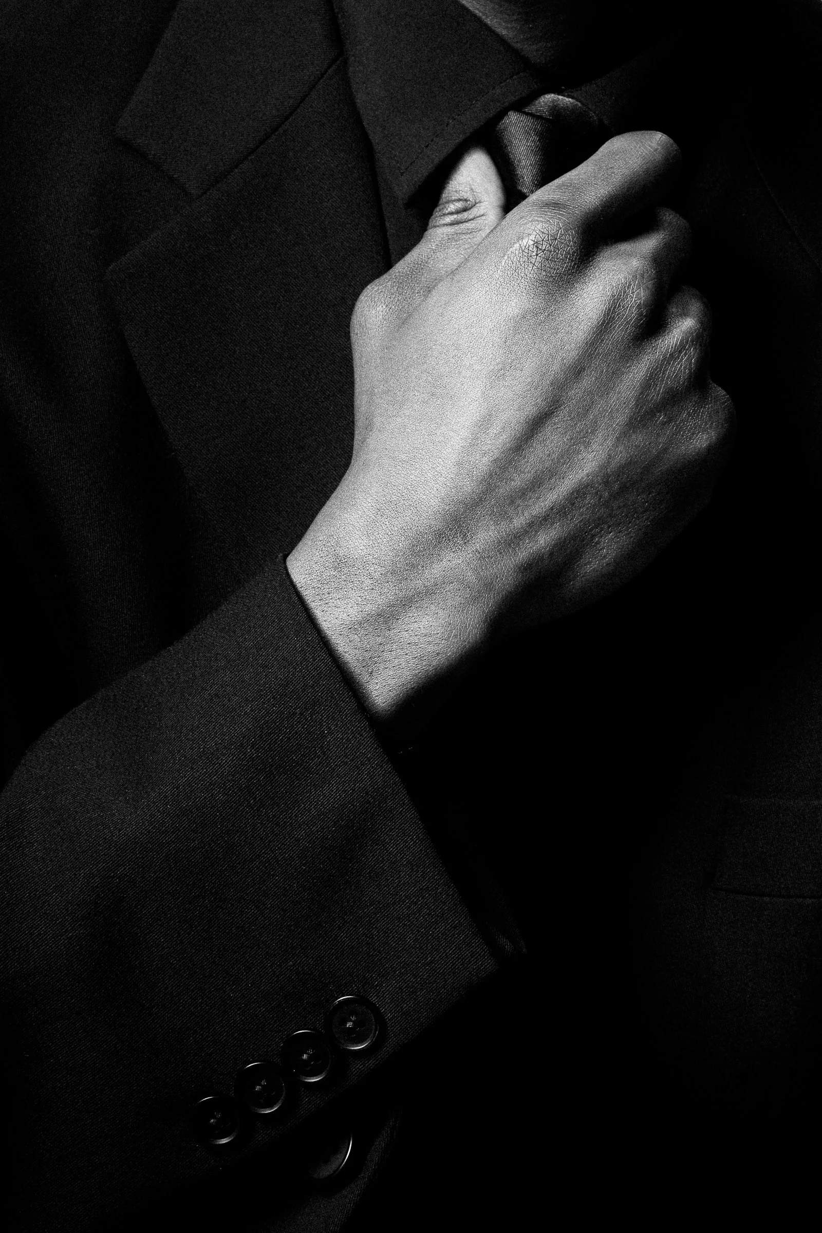 Premier plan d'une main masculine ajustant la cravate d'un homme habillé en costume noir formel.