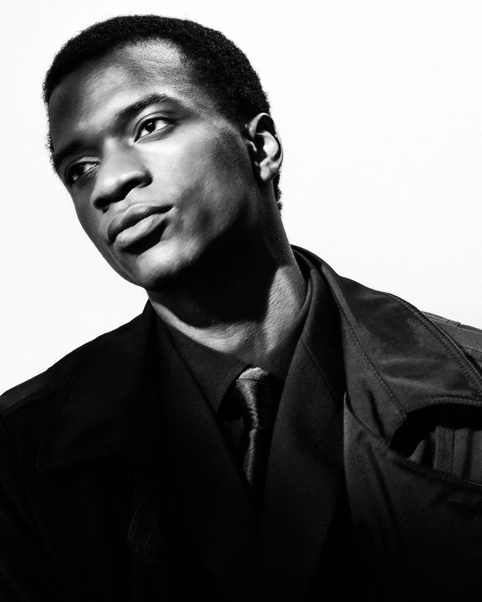 Portrait en noir et blanc d'un jeune homme avec des cheveux courts, portant une veste foncée, une chemise et une cravate, regardant légèrement vers la gauche.