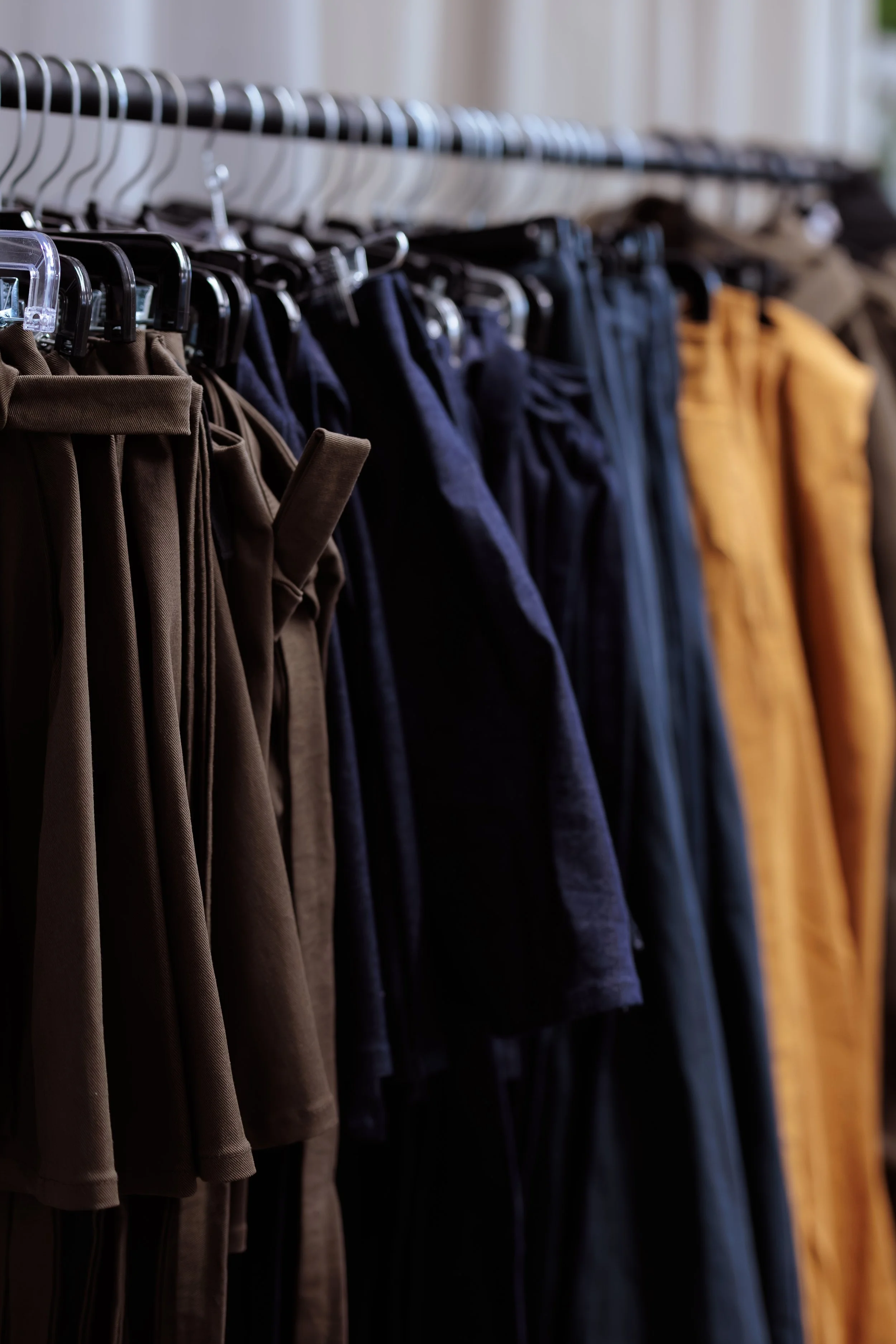 Vêtements pour hommes suspendus sur une planche dans un magasin, comprenant des pantalons beiges, bleus, noirs, et jaunes.