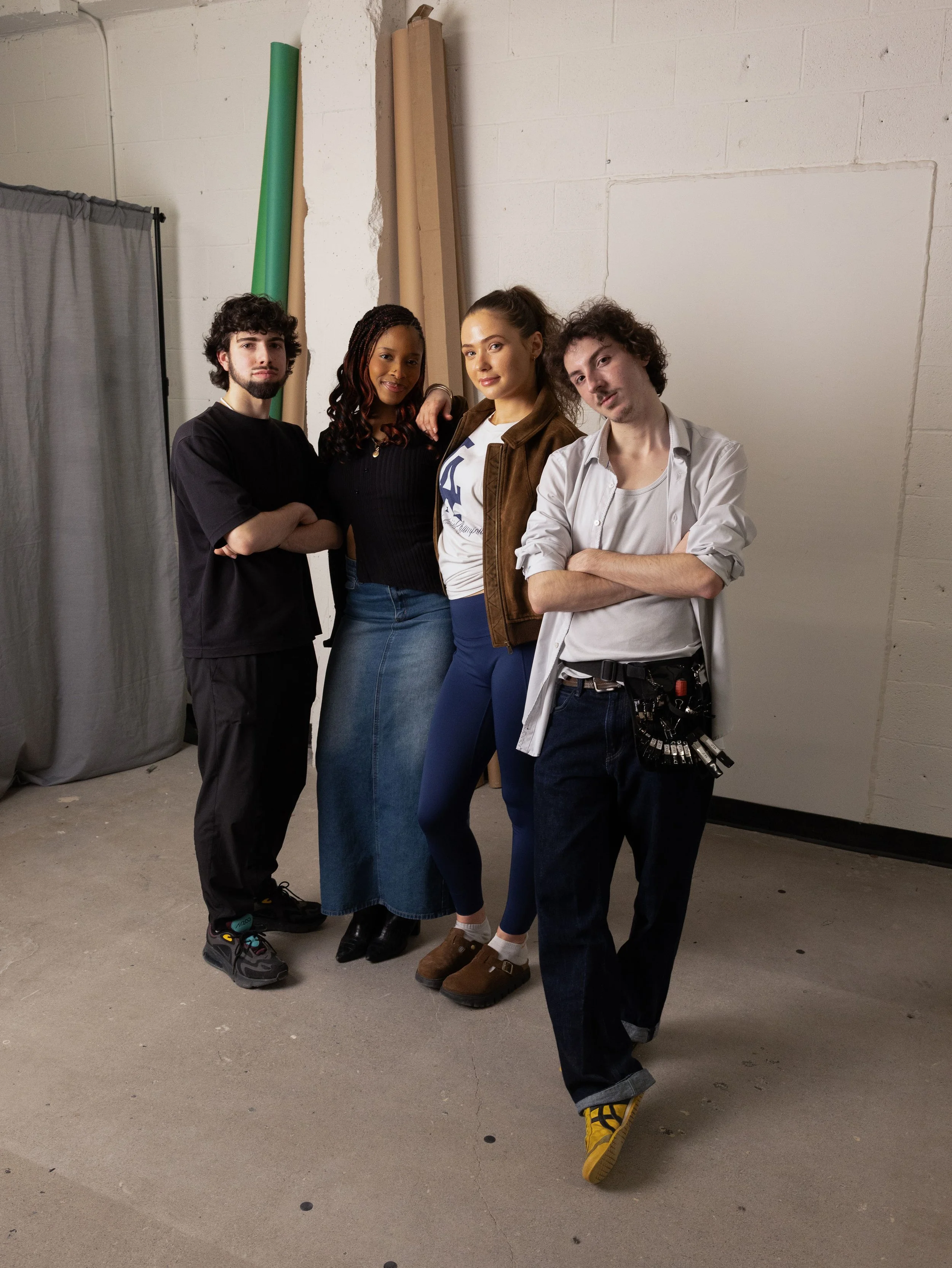 Quatre jeunes adultes posant pour une photo dans un studio, avec rouleaux de papier et rideaux en arrière-plan.