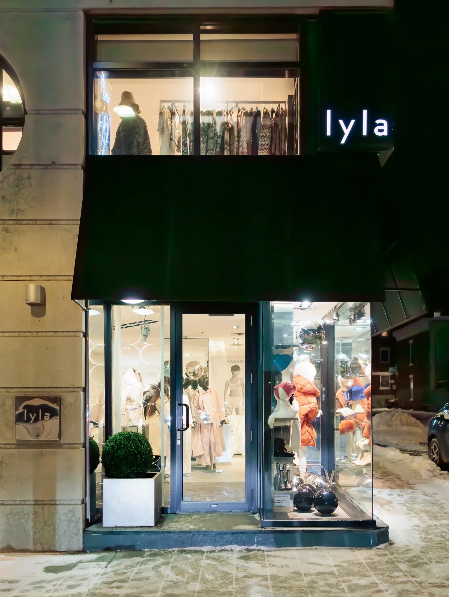 Vitrine d'un magasin de vêtements appelé Iyla, avec des mannequins et des vêtements visibles à l'intérieur, et un éclairage lumineux dans une ambiance de soirée ou de nuit.