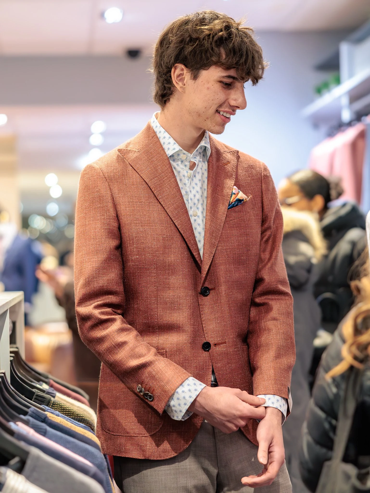 Un jeune homme en blazer marron clair regarde des vêtements dans un magasin.