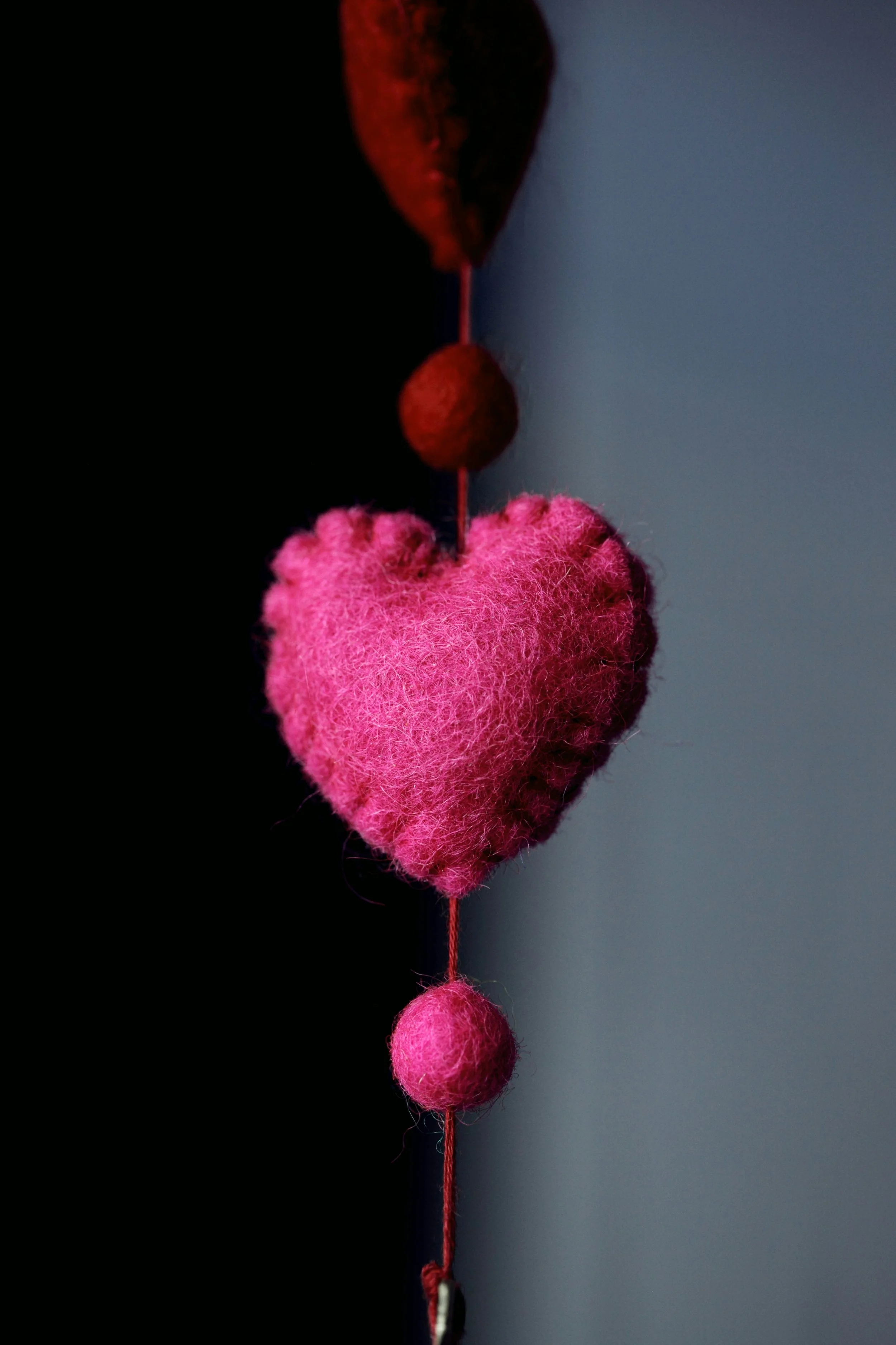 Pink felt hearts and balls hanging on a string against a blue wall.