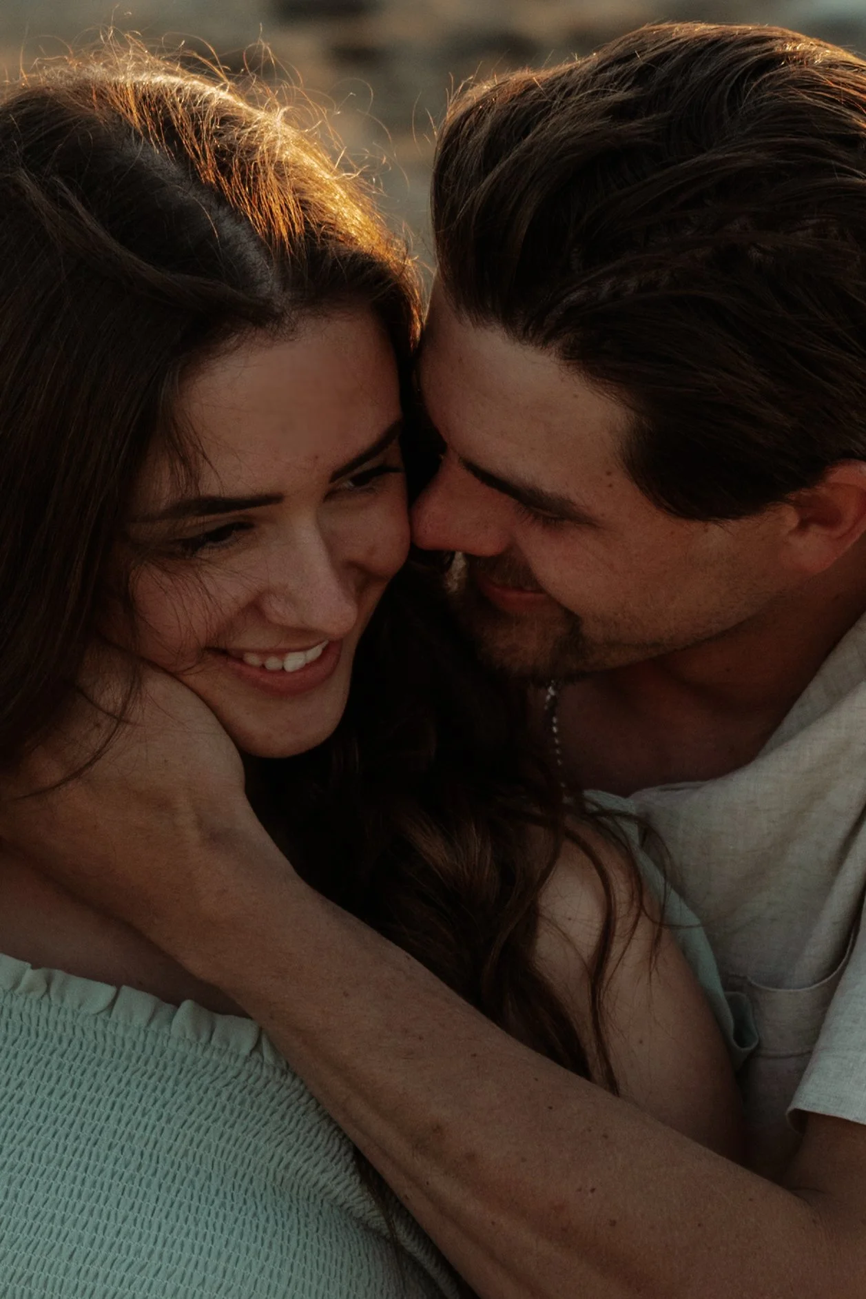 A couple sharing a close, intimate moment, smiling and leaning their faces towards each other, with warm sunlight illuminating their faces.