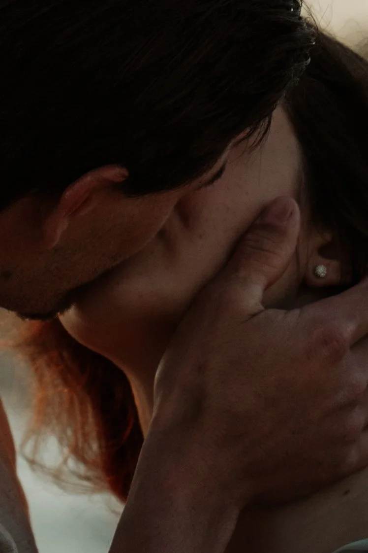 A close-up of a person kissing another person's cheek, with both having a hand on the face being kissed.