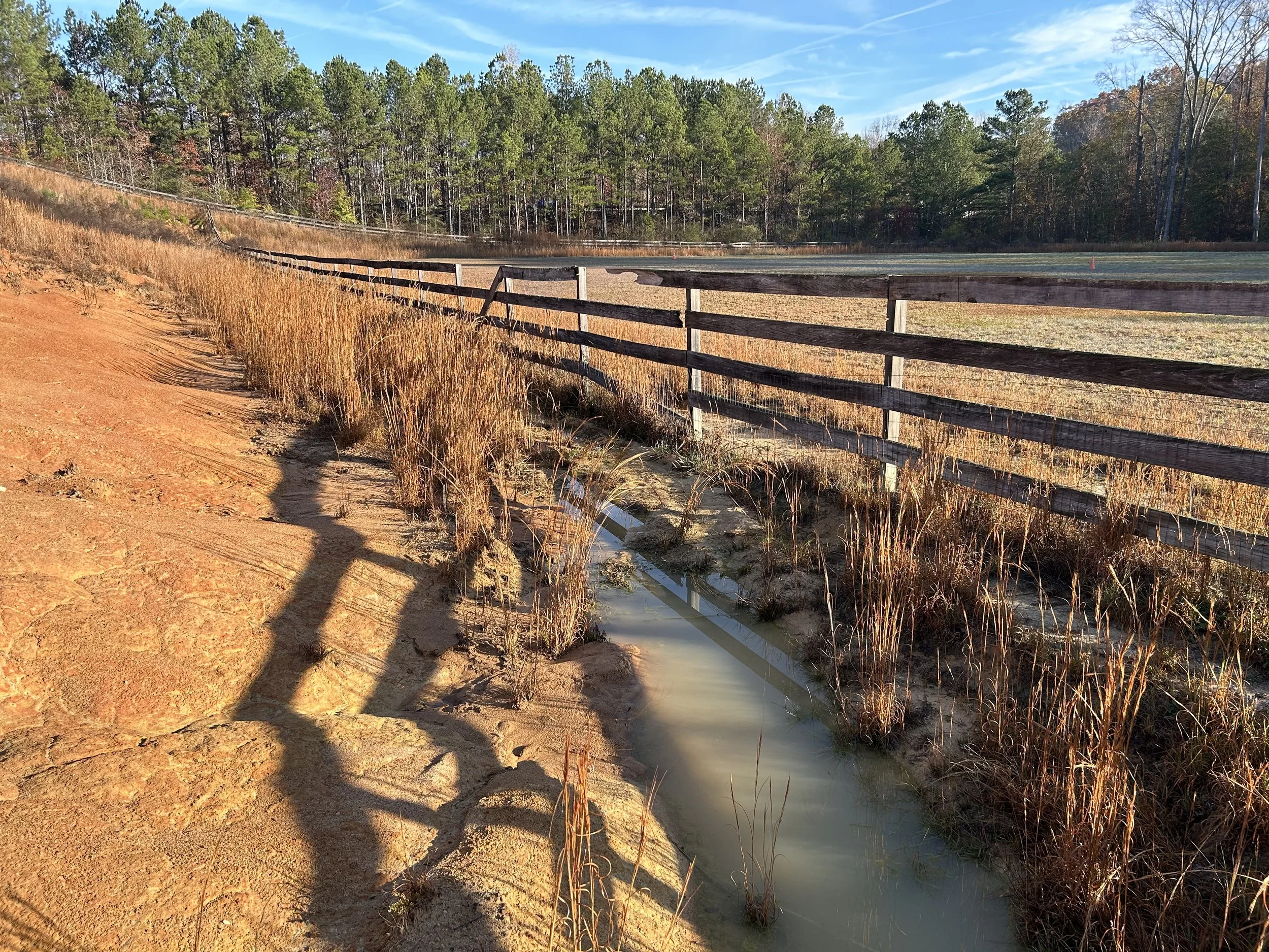 Standing water and erosion along existing drainage path beside pasture fencing before reconstruction