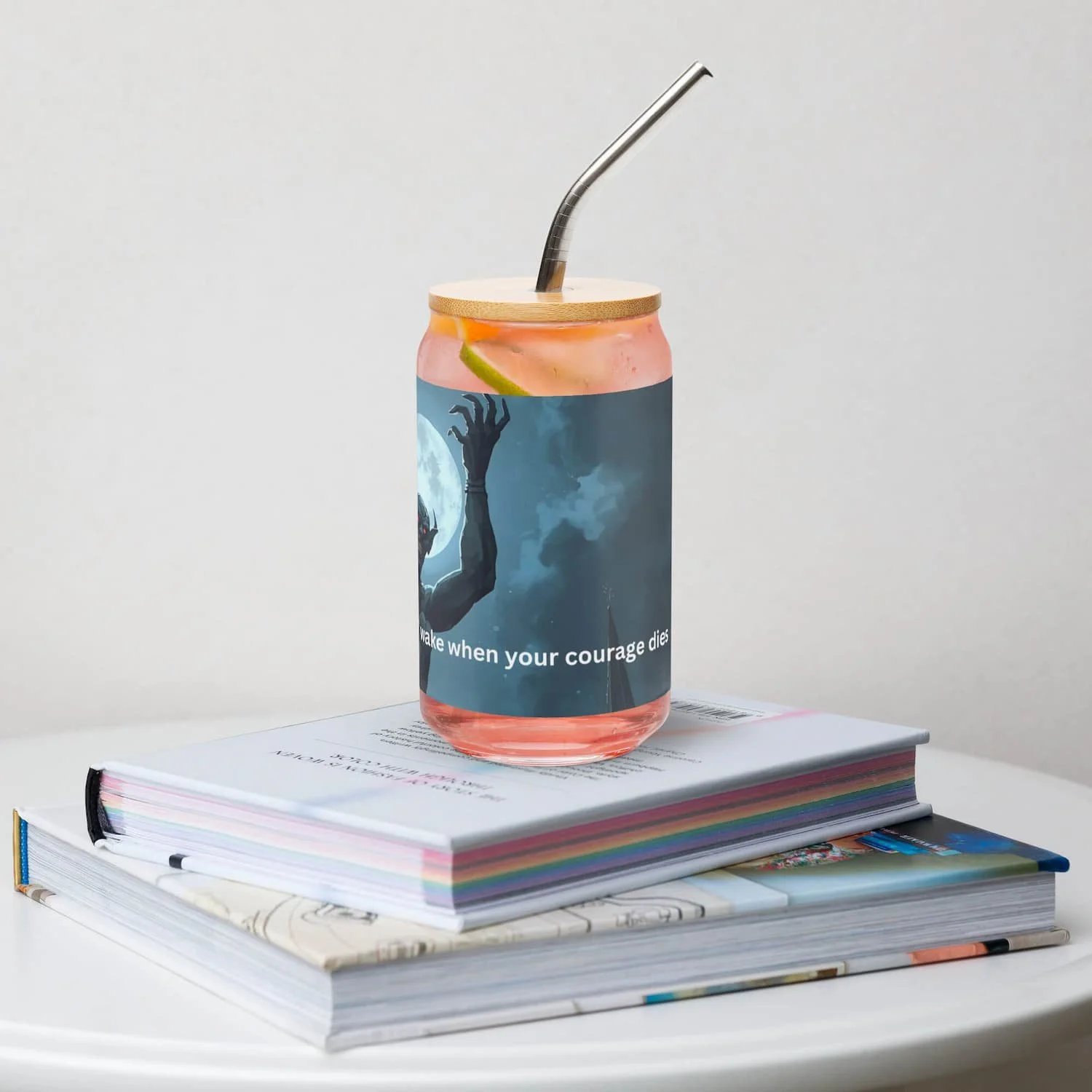 Left view of 16 oz can-shaped glass with lid and straw on a book on a table