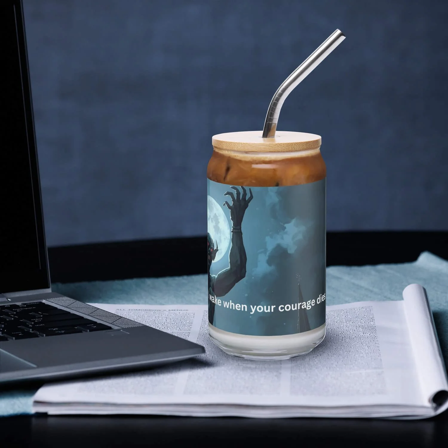 16 oz can-shaped glass with lid and straw sitting on a table next to a laptop, left side view, clear reusable drinkware cup