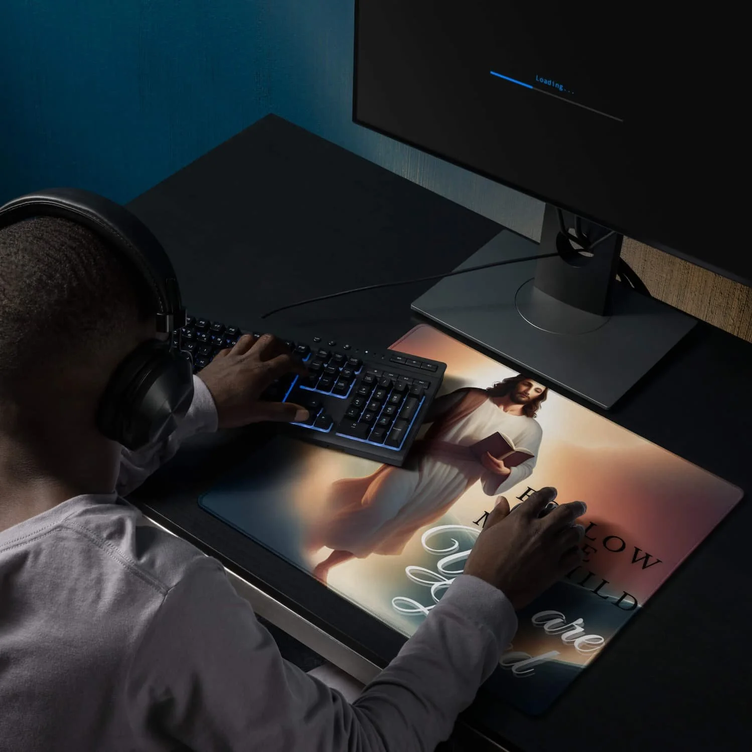 Man playing at his desk using an extended gaming mouse pad featuring Jesus walking in the clouds with the message “Follow Me My Child,” shown with a keyboard and mouse on the mat