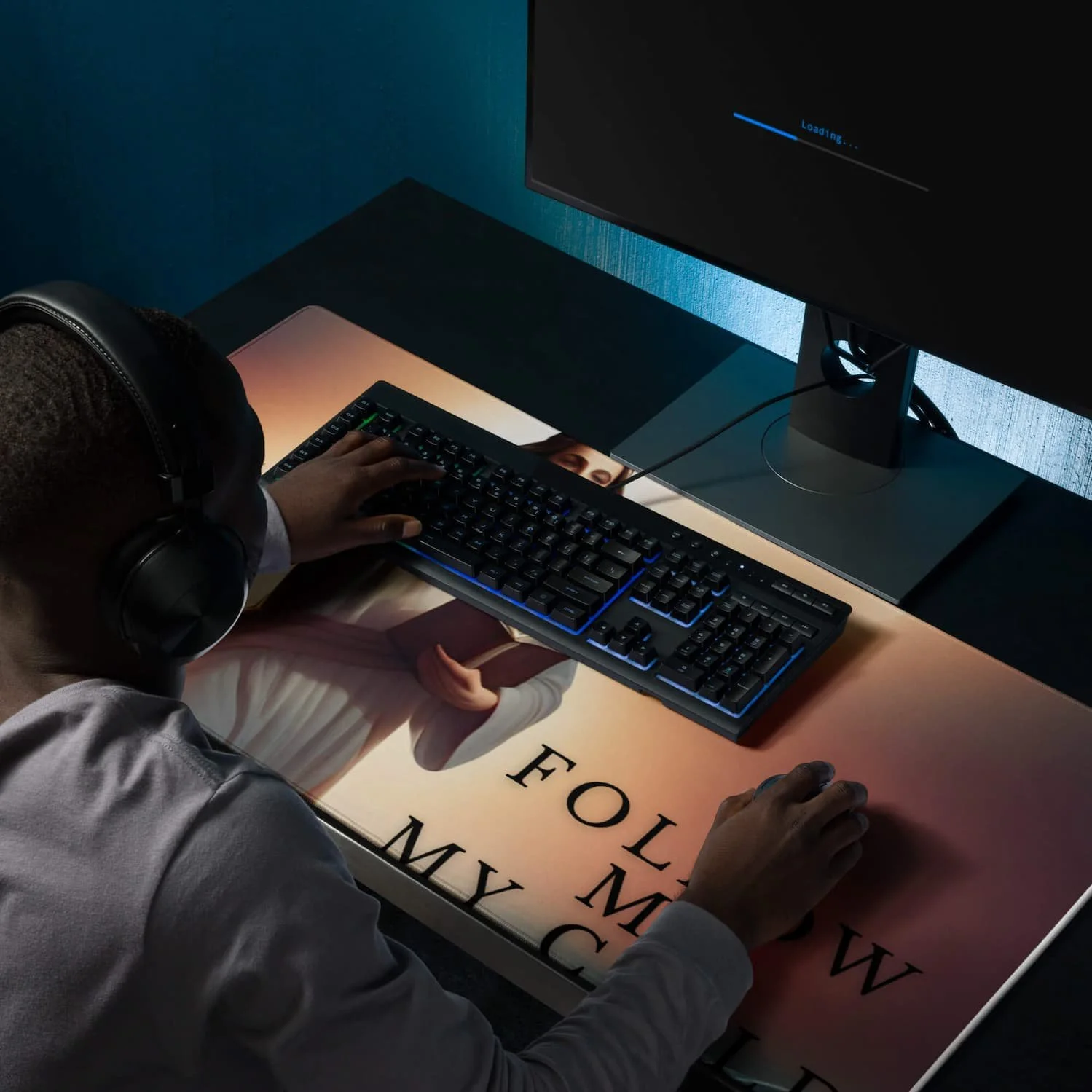 Man playing at his desk using an extended gaming mouse pad featuring Jesus walking in the clouds with the message “Follow Me My Child,” shown with a keyboard and mouse on the mat