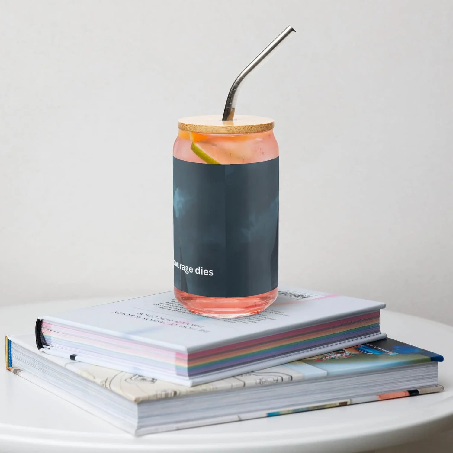 16 oz can-shaped glass with lid and straw sitting on a book on a table, back view, clear reusable drinkware cup