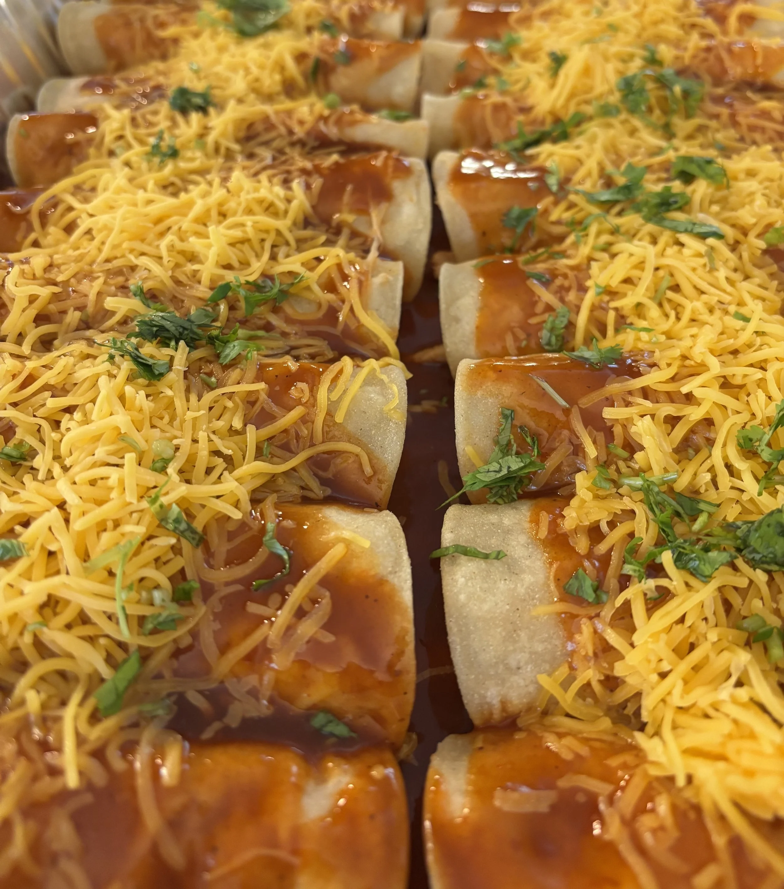 Four rows of mini tacos topped with shredded cheese, chopped herbs, and sauce.