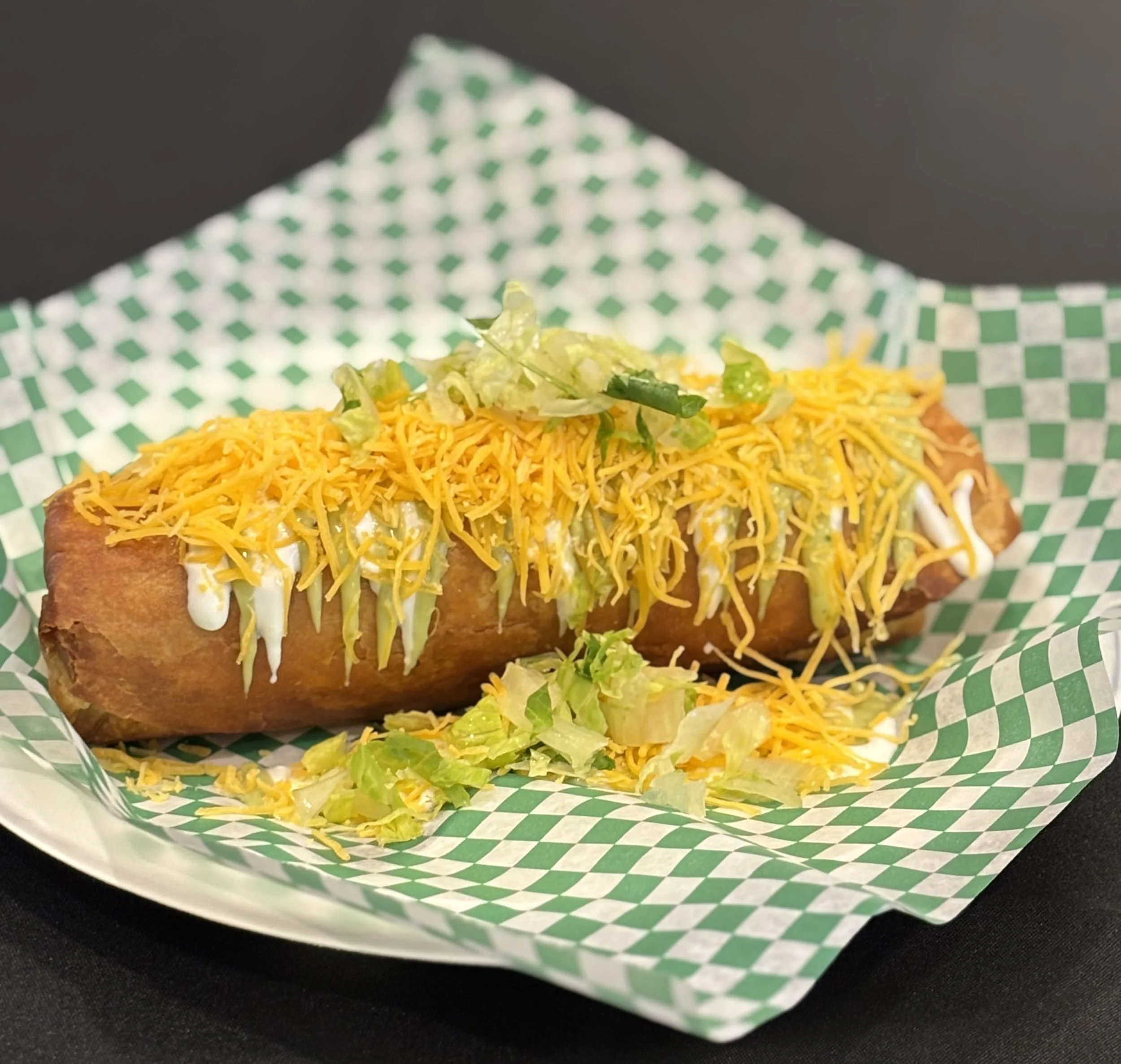 Chili cheese hot dog with shredded cheese, shredded lettuce, and mayonnaise on a paper-lined basket.