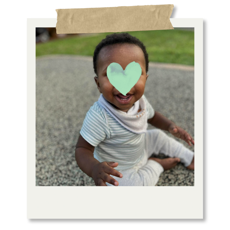 Niño sonriendo sentado en el suelo con una cara cubierta con un corazón de color verde claro.