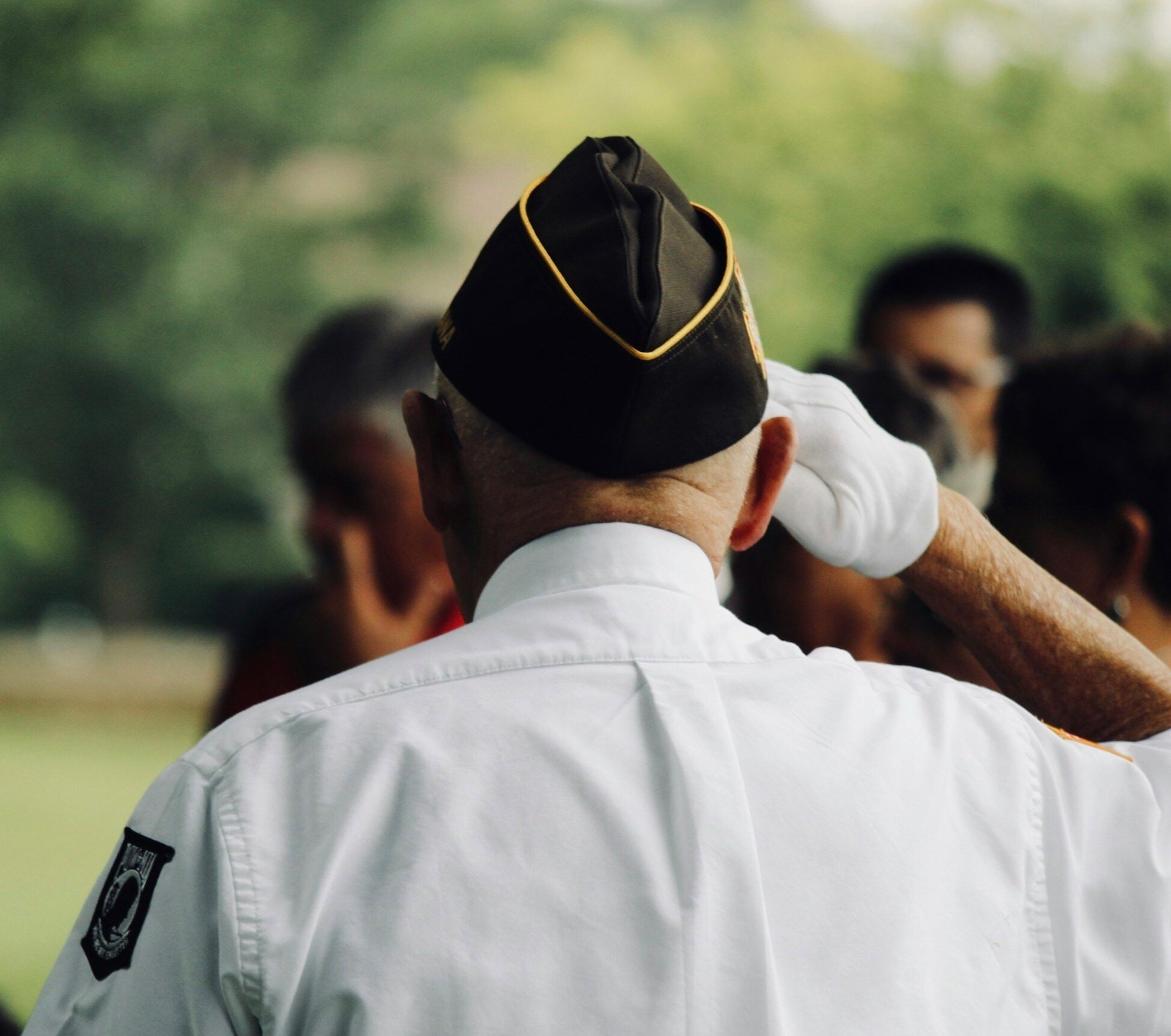 Veteran in uniform saluting during an outdoor gathering, representing honor, respect, and faithful service.