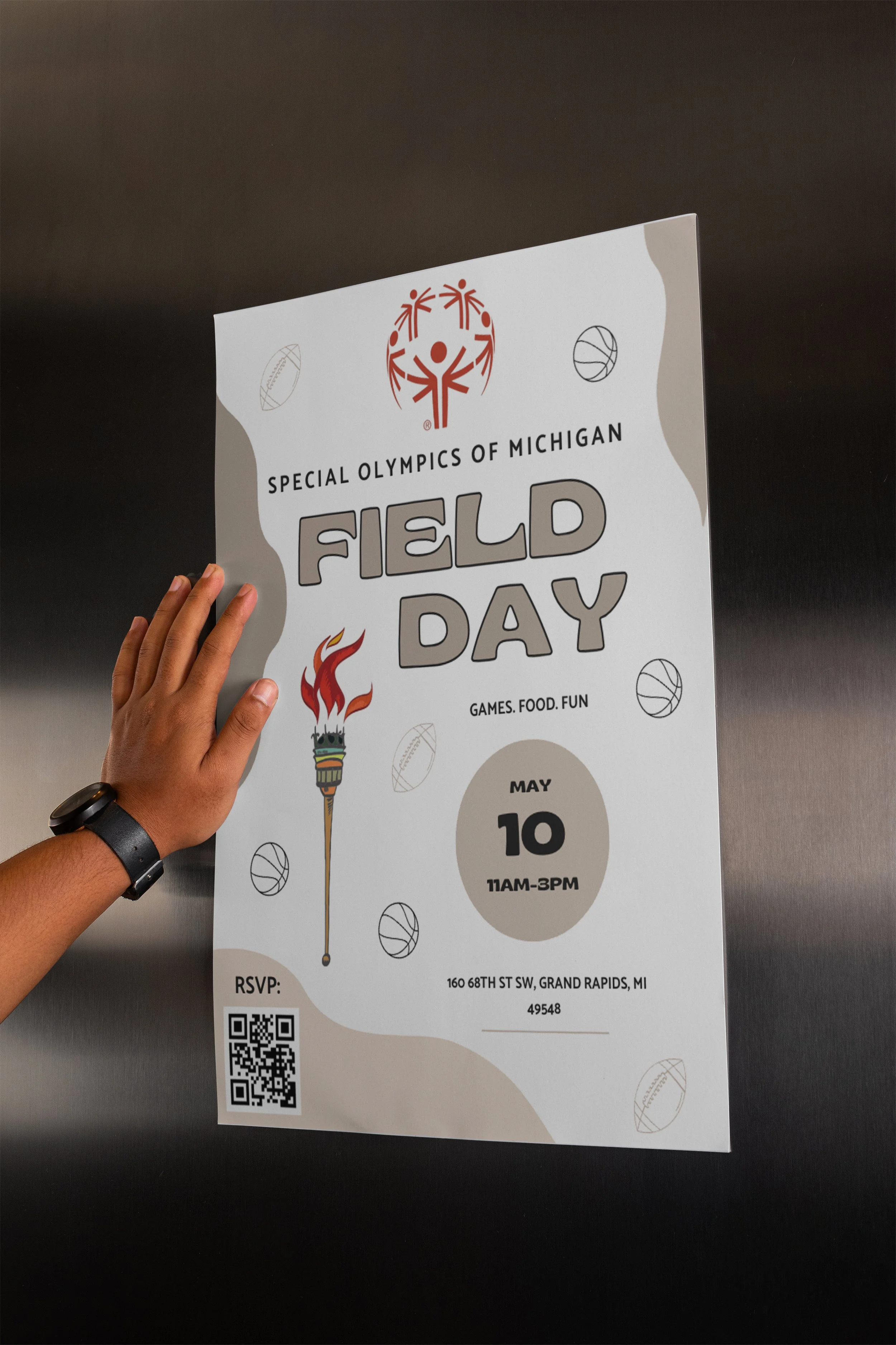 A person’s hand holding a poster for the Special Olympics of Michigan Field Day event, featuring sports illustrations and event details including date, time, location, and RSVP QR code.