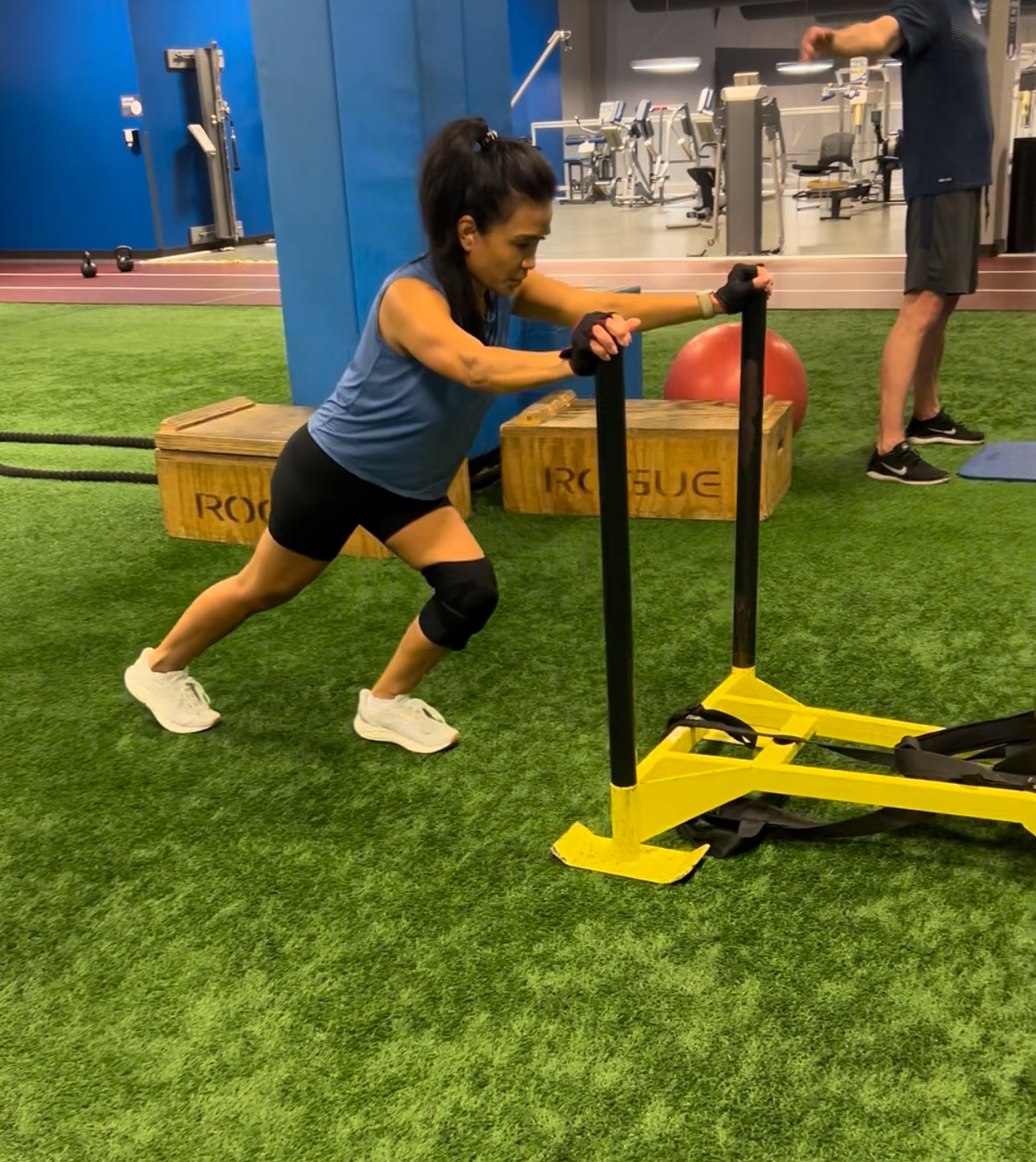 Woman pushing sled with resistance bands in a gym.