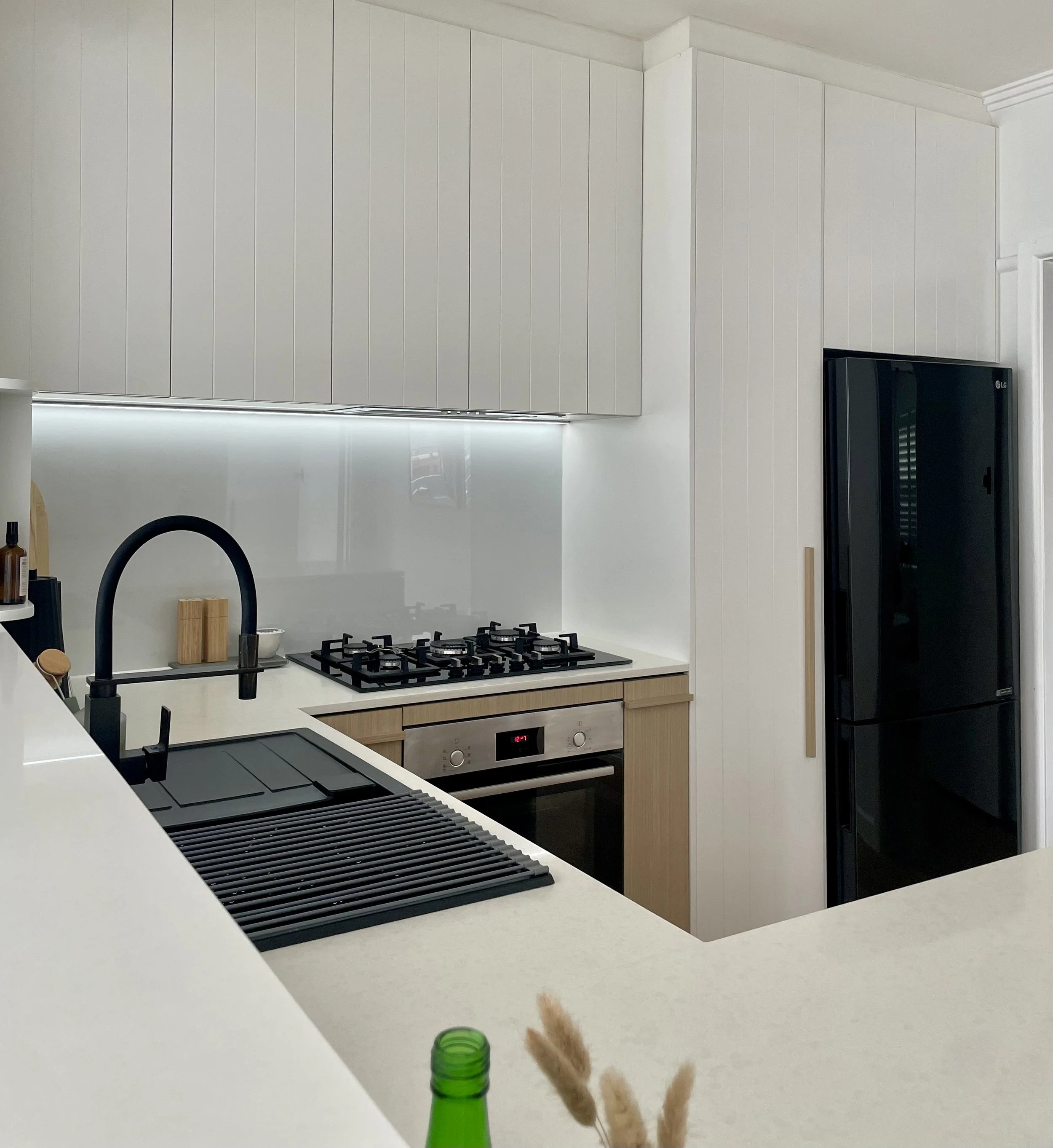 Kitchen renovation with linear white cbinets and 2 pack painted finish. V-groove to doors and timber grain base joinery. Black flexible hose