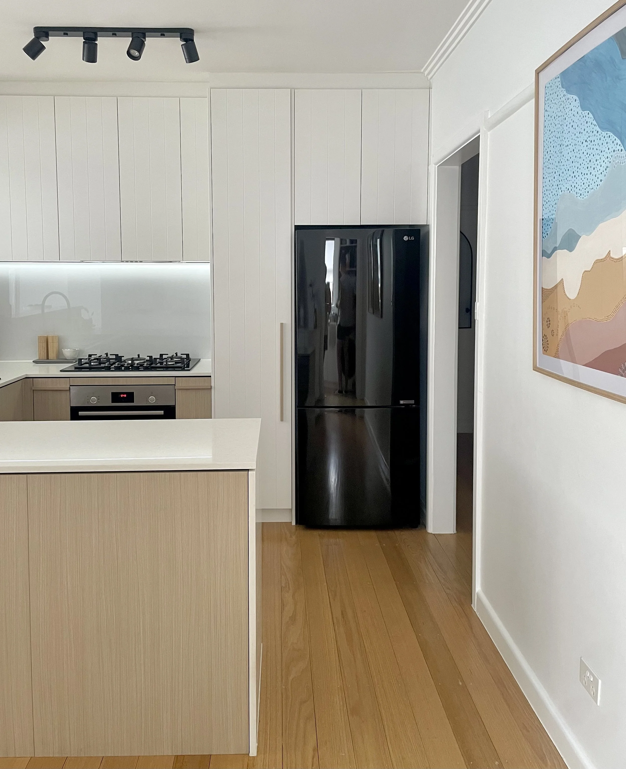 Kitchen renovation in old Melbourne home with silica free white stone benchtops, black fridge, laminatex metaline spashback and white painted doors. Timber look laminate cabinet doors and hardwood timber flooring