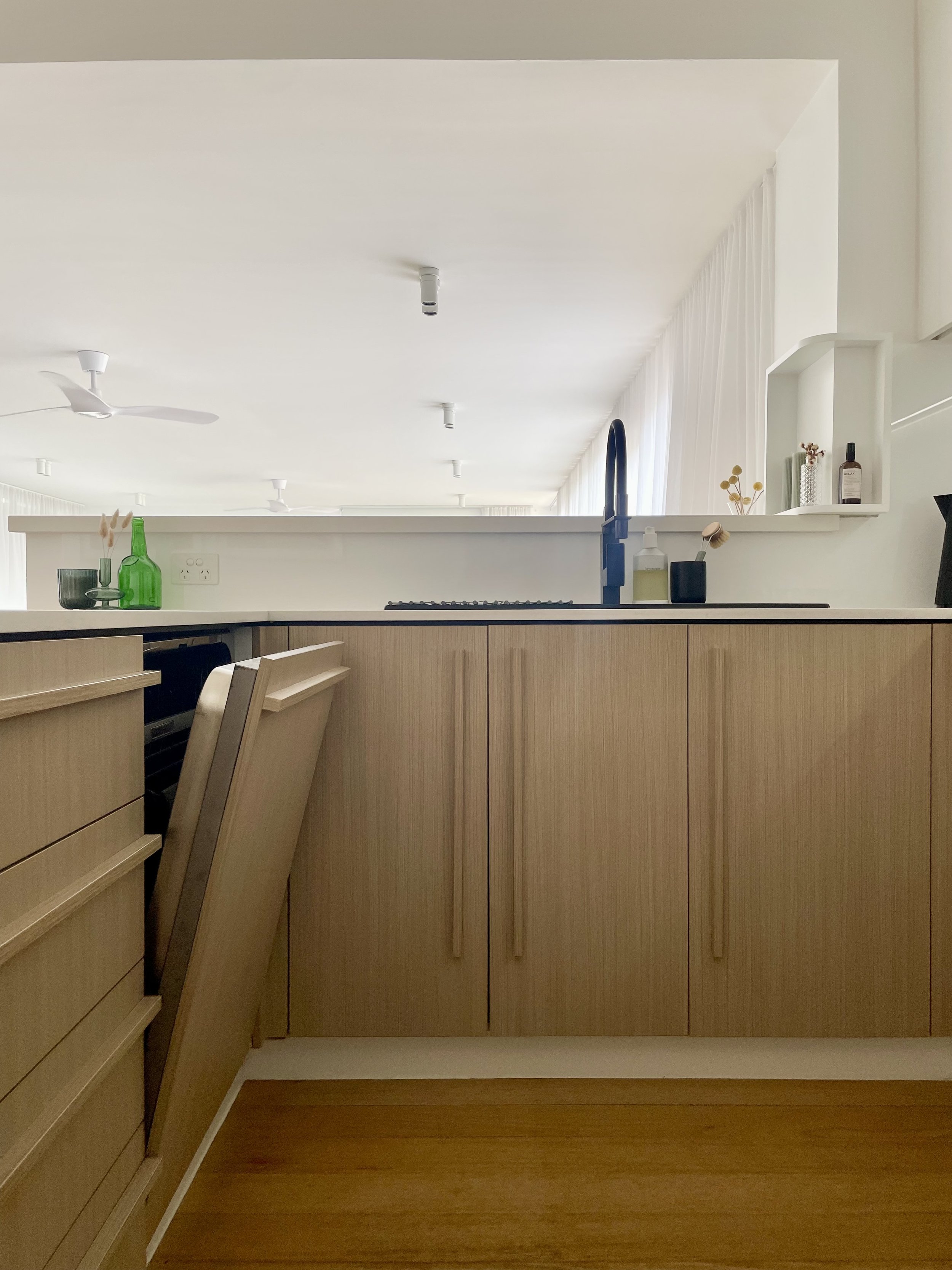 Kitchen renovation with timber laminate doors and elegant door handles. Integrated dishwasher with pull handle and black faucet. white fan and elegant ikea white spotlights