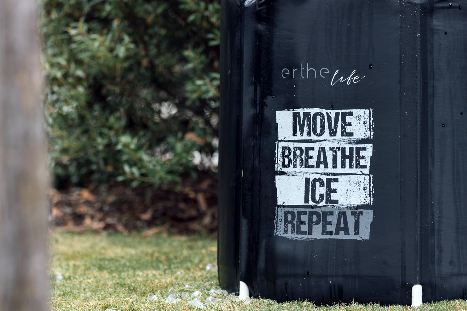 A black outdoor ice bath with the phrase "MOVE BREATHE ICE REPEAT" written in bold, distressed white and gray text.