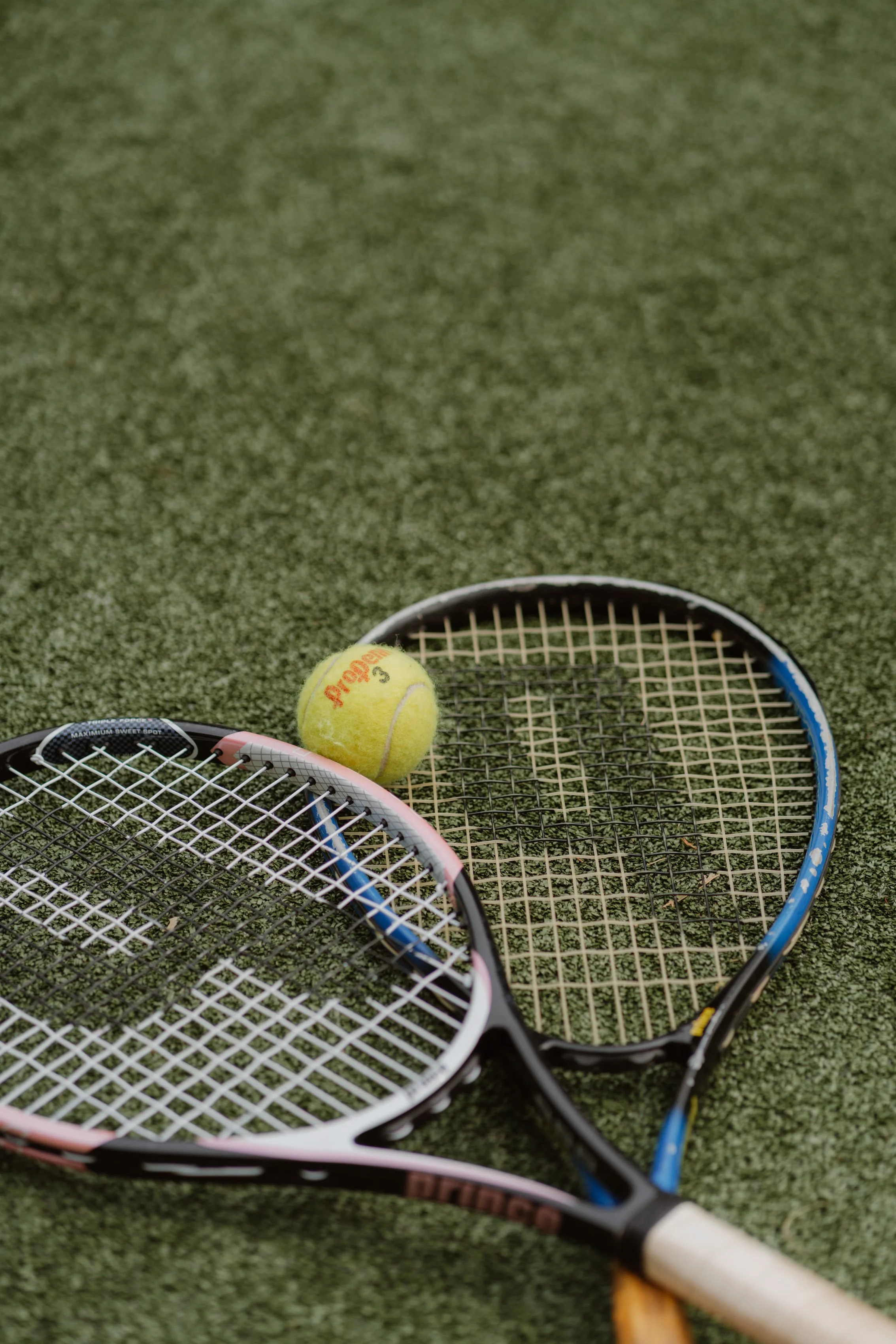Two tennis rackets and a tennis ball on a green tennis court