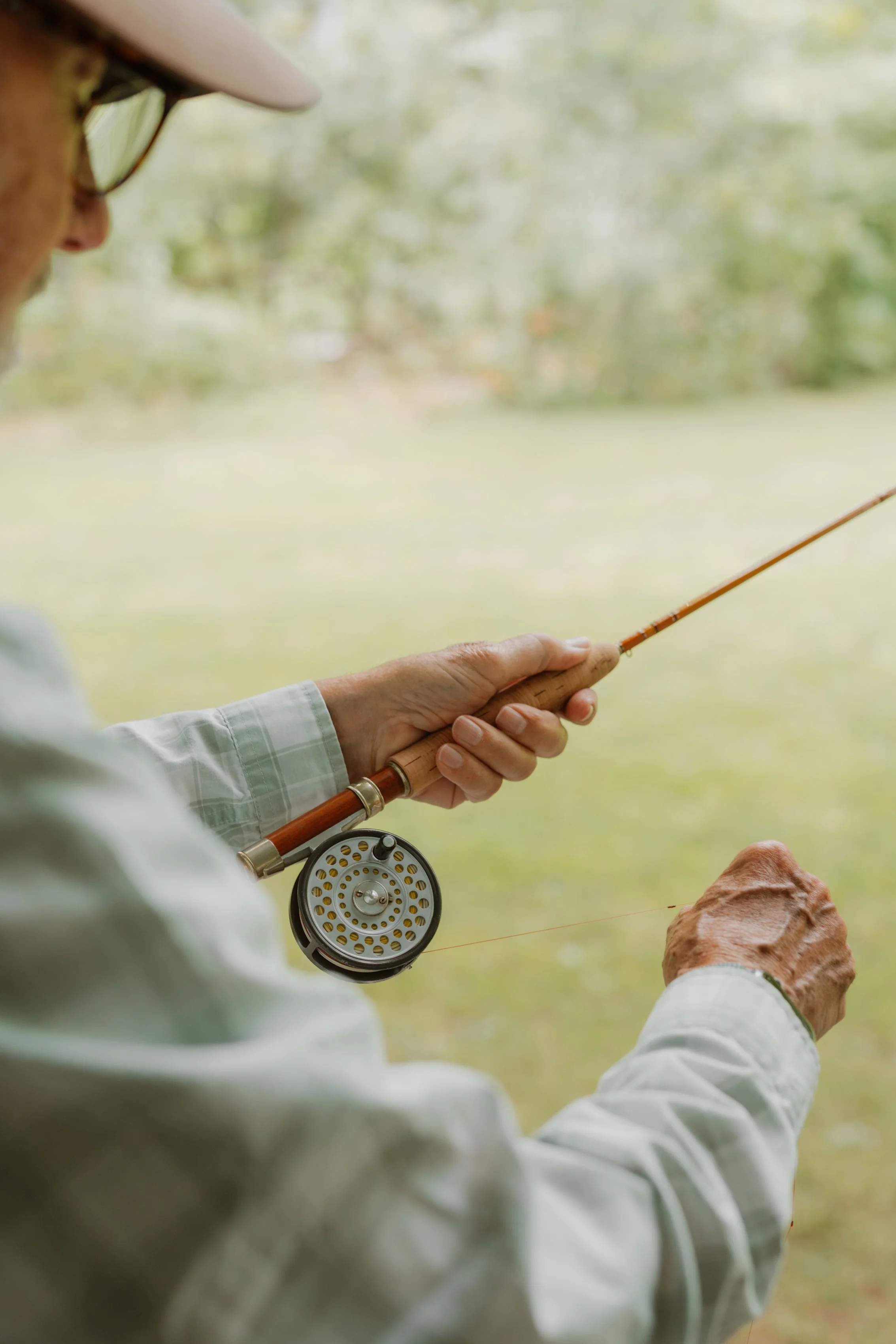 Person holding a fly fishing rod near a lake or river.