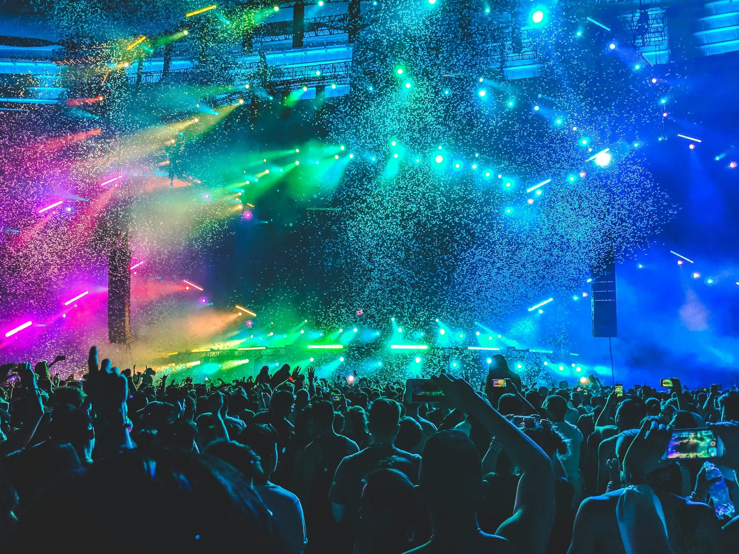 Crowd at a concert with colorful stage lights and confetti falling.