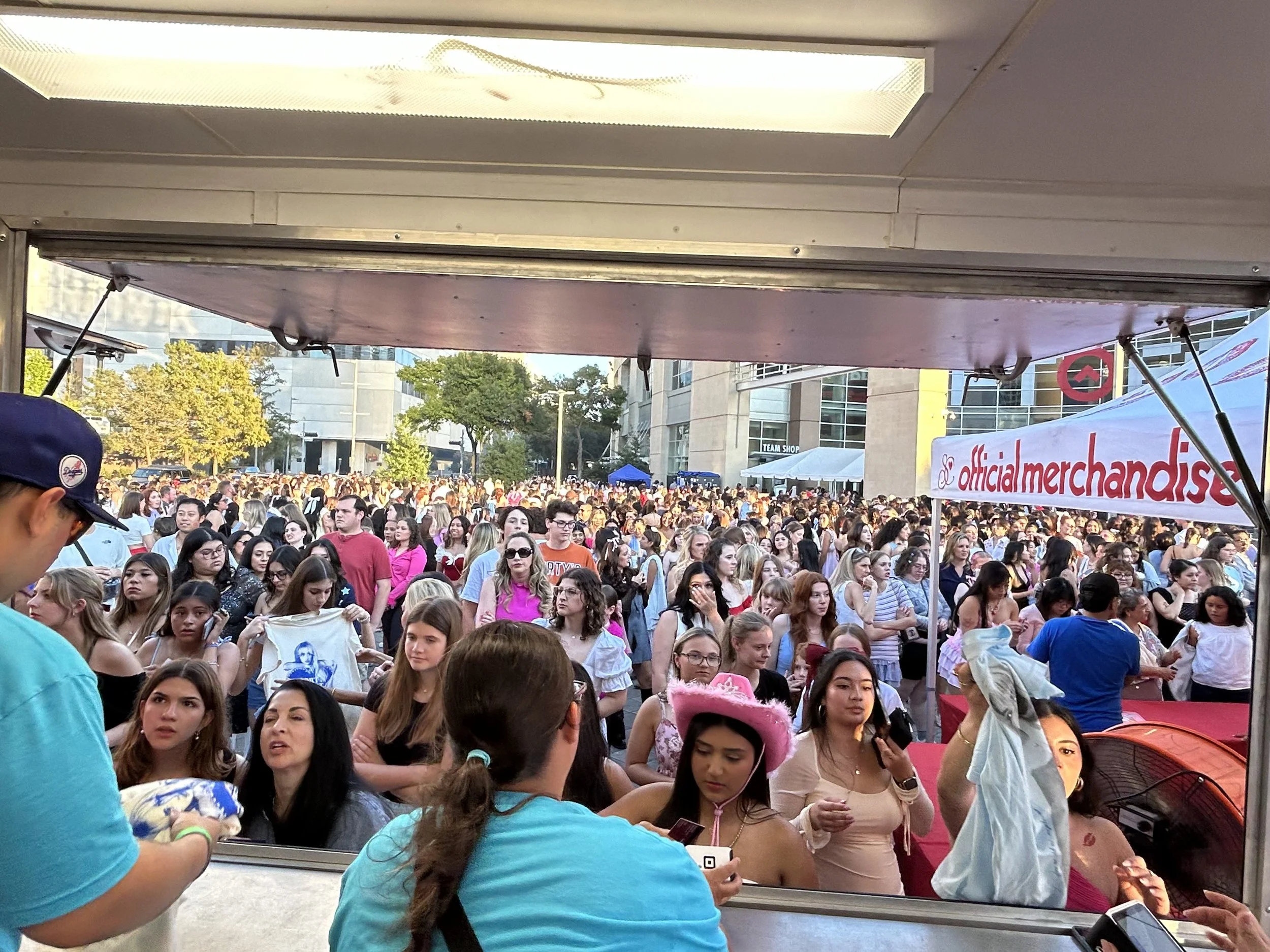 Crowd of people at an outdoor event viewed from a vendor booth window.