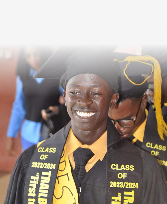 A smiling young man in graduation cap and gown, with a yellow sash and honor cord, celebrating graduation with classmates.