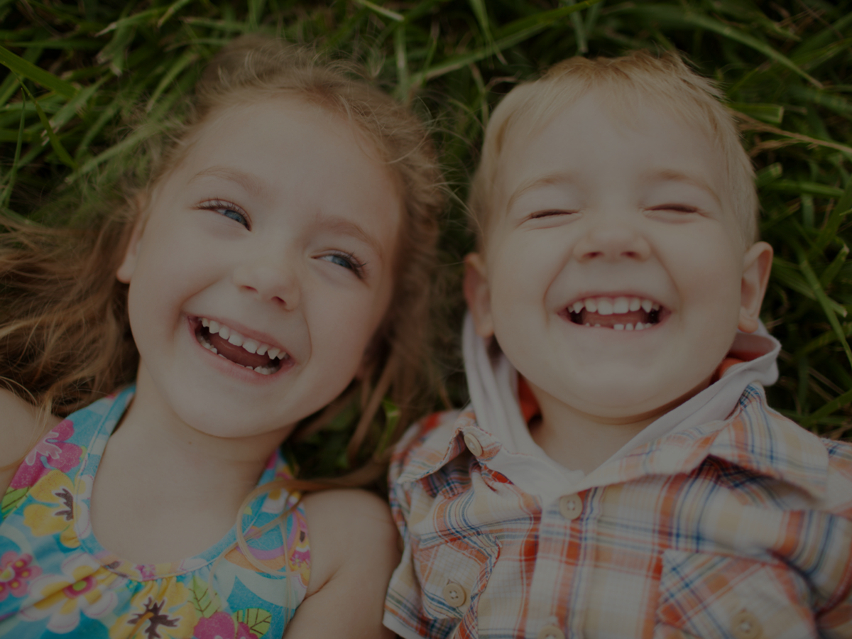 Two happy children lying in the grass, smiling and showing healthy teeth