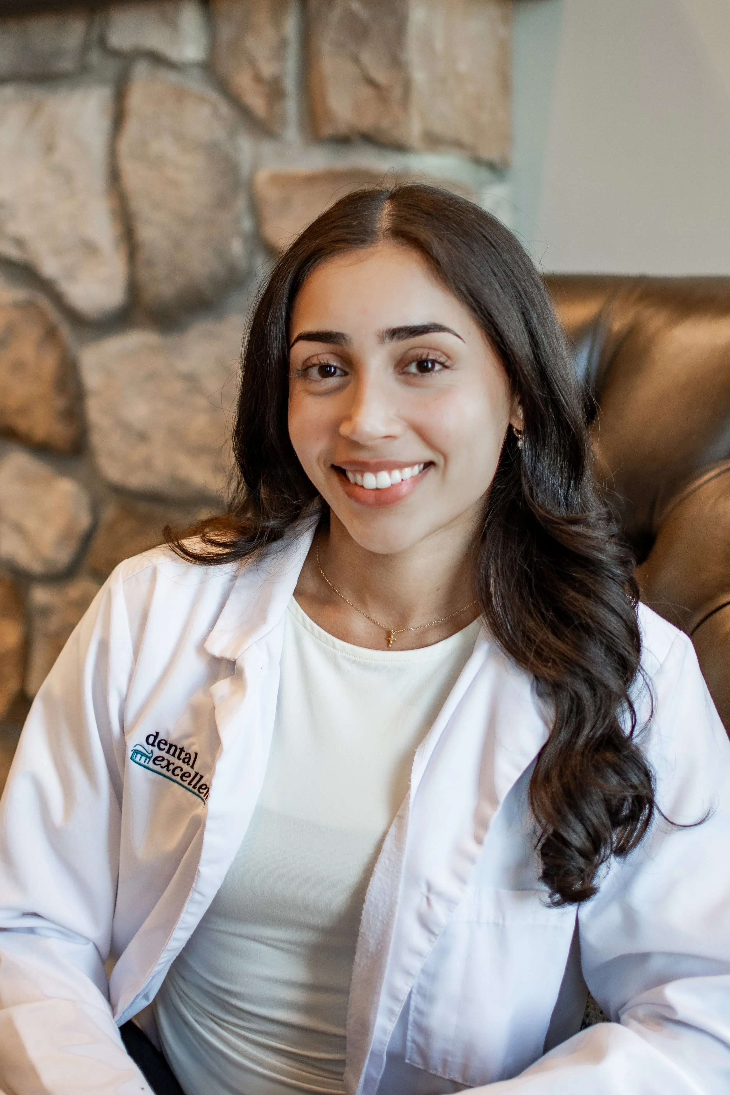 Dr. Dina Desai smiles while wearing a Dental Excellence lab coat in the office, providing comprehensive family and general dentistry for patients in Northwest Ohio.