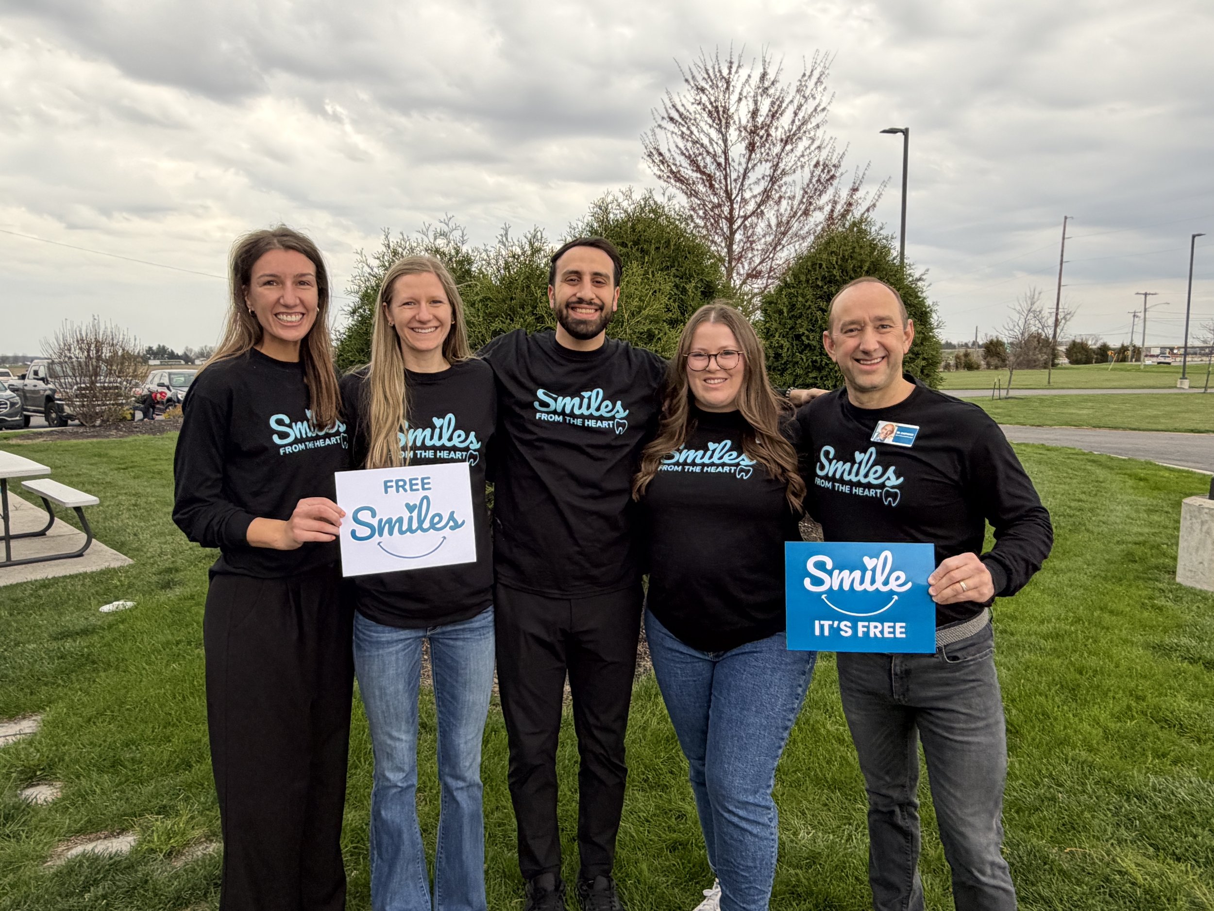 Dental Excellence team members at Smiles From the Heart holding signs for free dental care community outreach