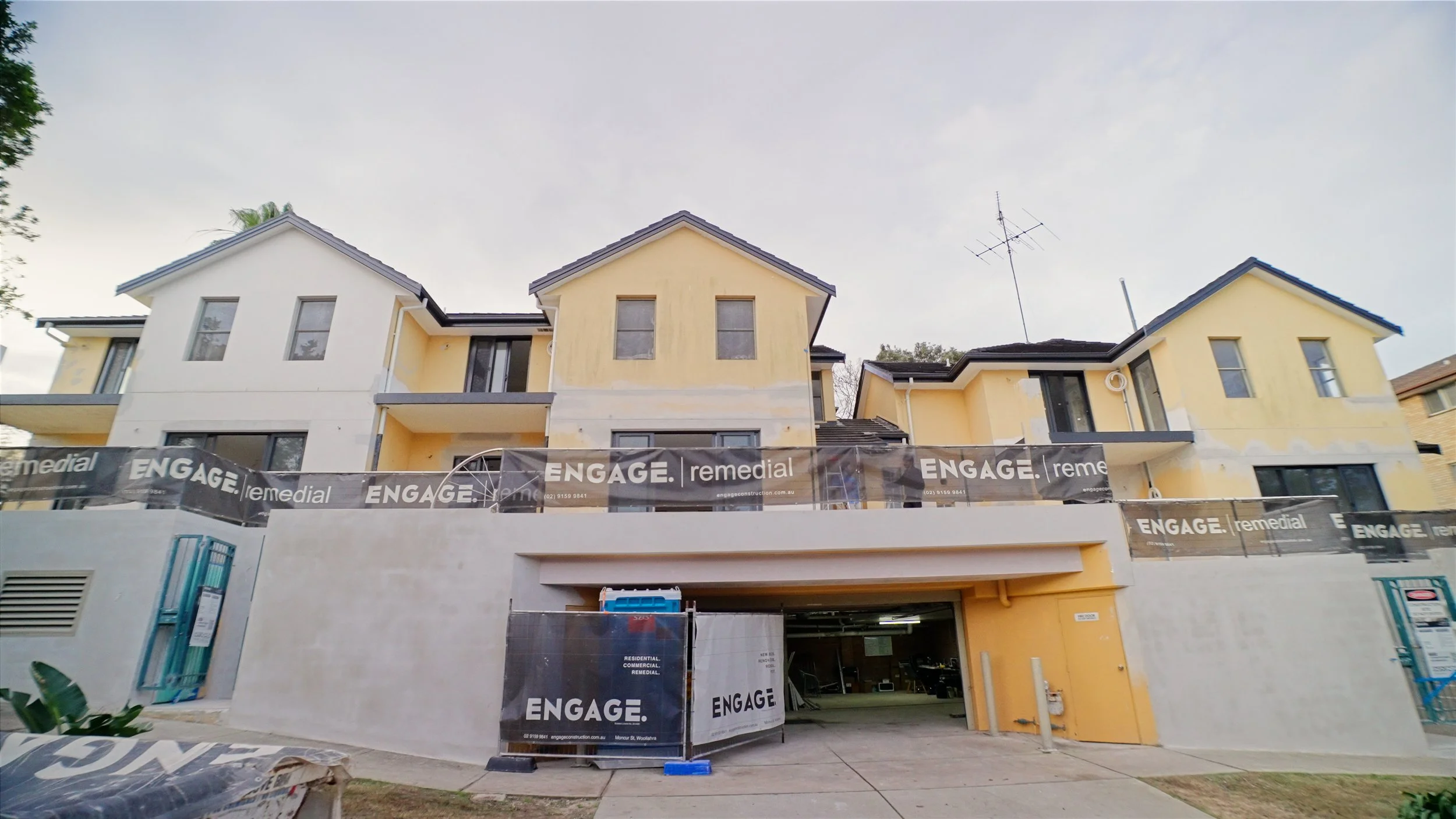Under construction multi-story residential building with yellow and white exterior walls, scaffolding, and building signs that say 'ENGAGE' and 'remedial'.