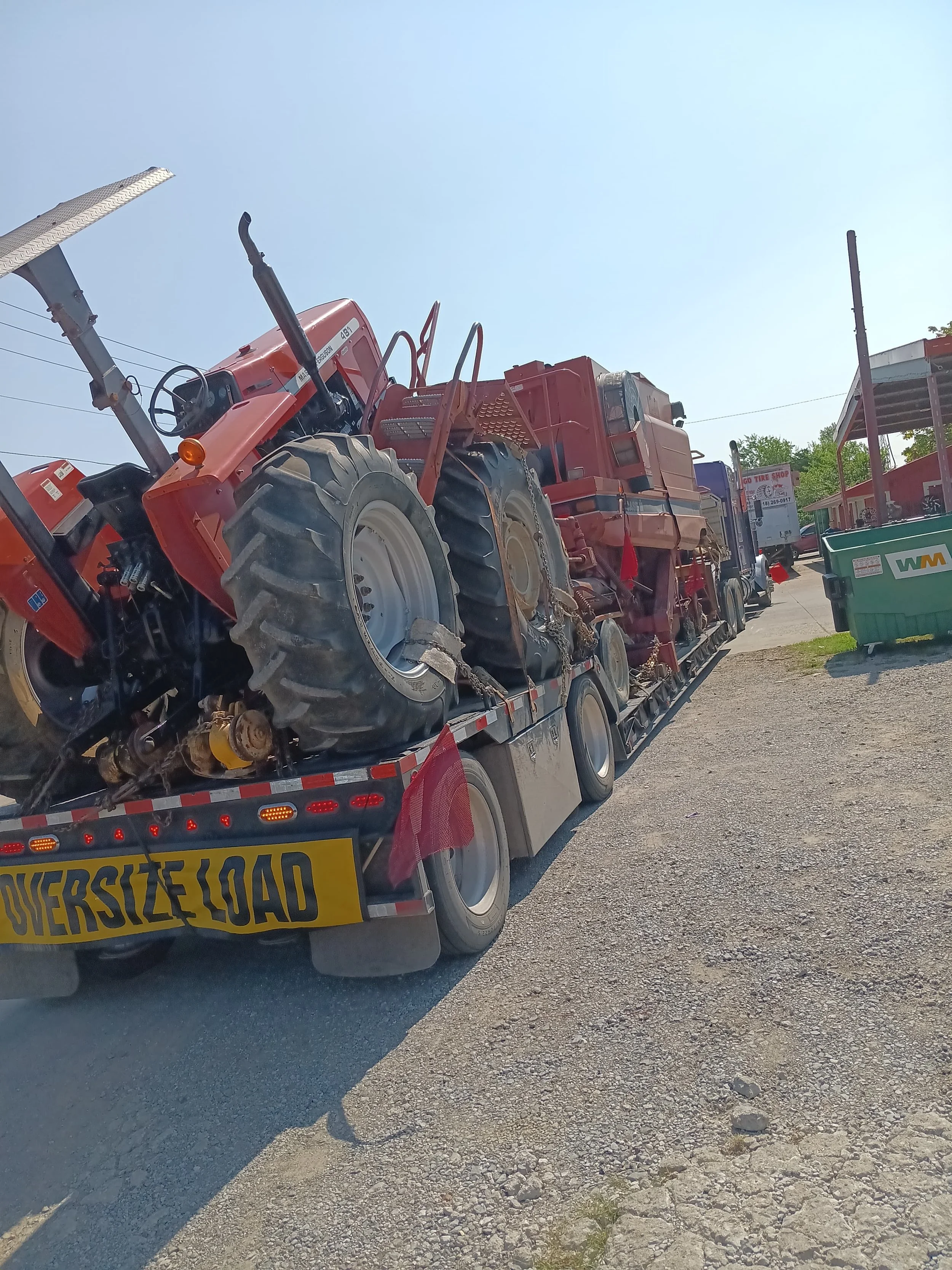 A flatbed truck carrying multiple red tractors on a gravel surface under a clear blue sky.
