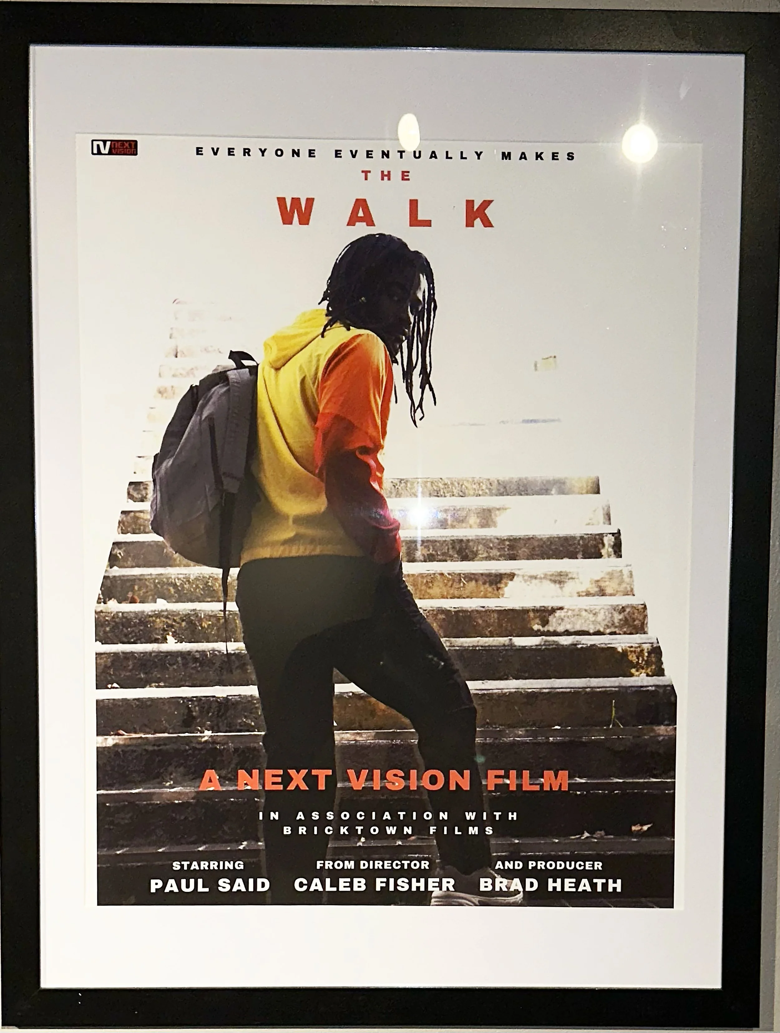 Poster for the film "The Walk" featuring a young person with dreadlocks wearing a yellow and red jacket, carrying a backpack, standing on stairs.