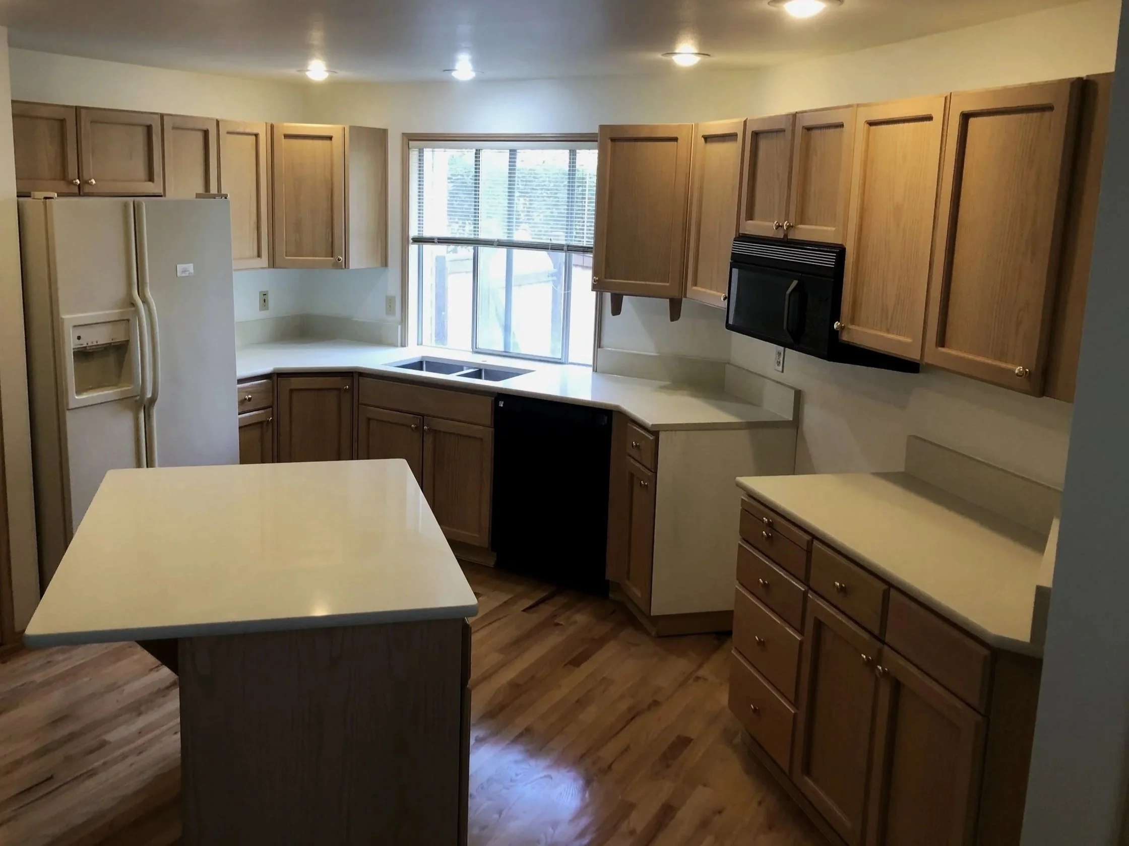 A kitchen with wooden cabinets, a white refrigerator, a window with blinds, and a kitchen island with a light-colored countertop.