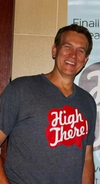 Man wearing a navy T-shirt with red and white text that says 'High There!'