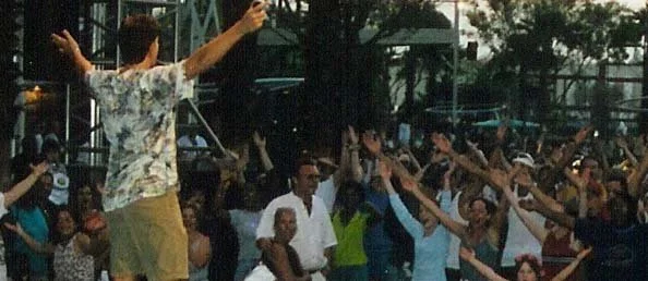 Man standing on a raised platform leading an outdoor group exercise class.