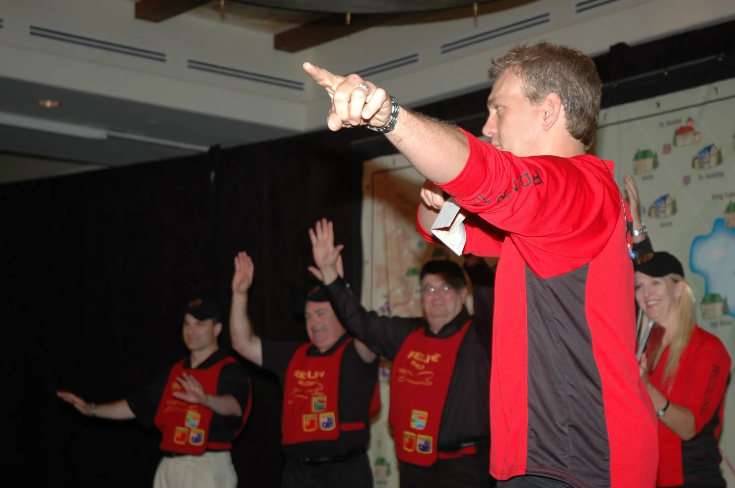 Mitch Mitchem on stage pointing to the audience, team in red Reliv vests behind him