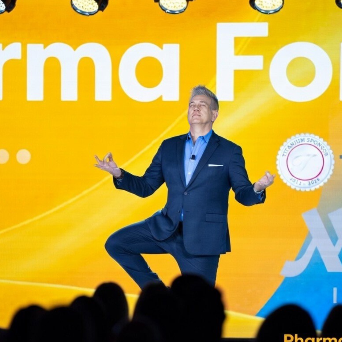 Mitch Mitchem on stage at Informa Pharma Forum, hands raised, energizing a room of delegates