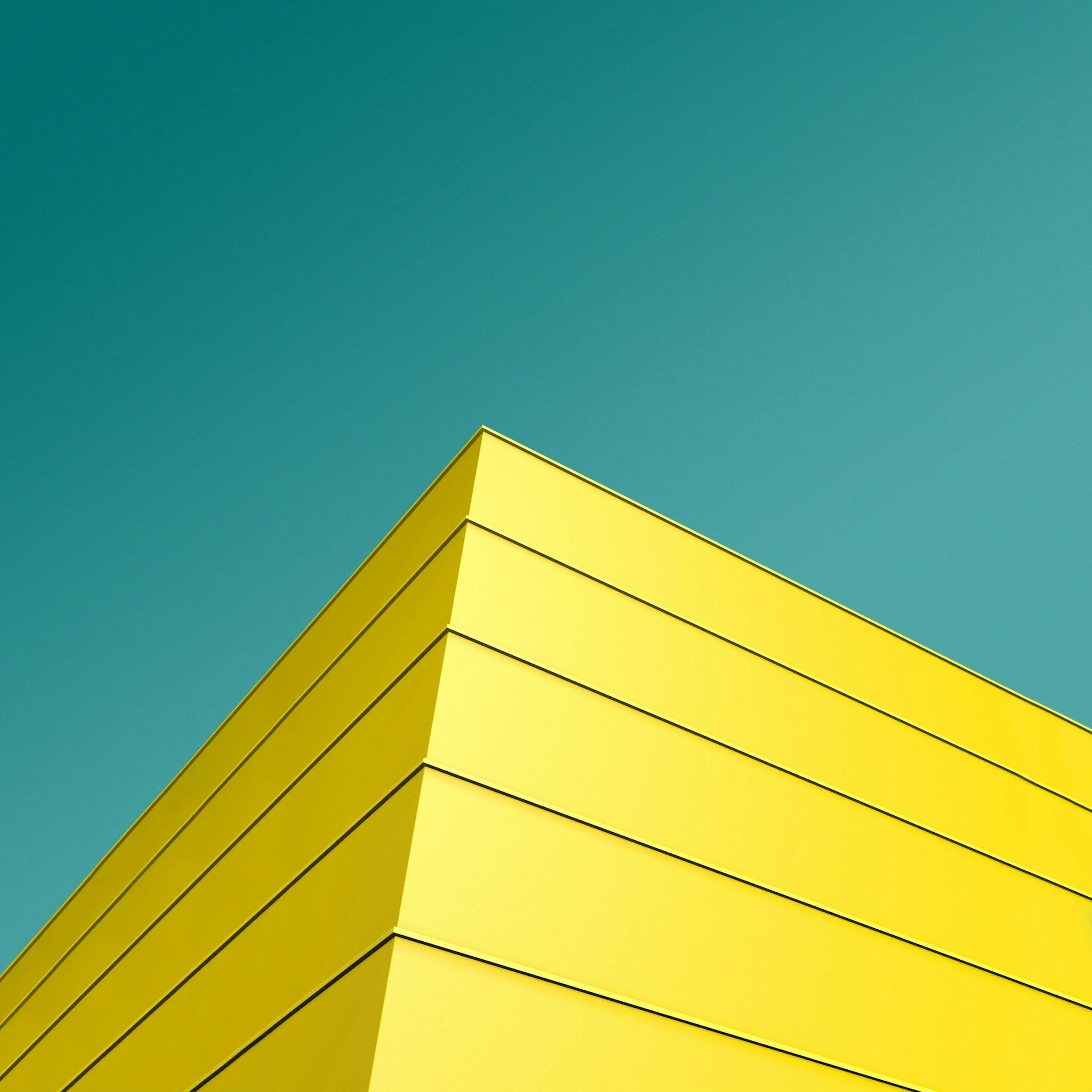 Yellow geometric building corner against a turquoise sky background.