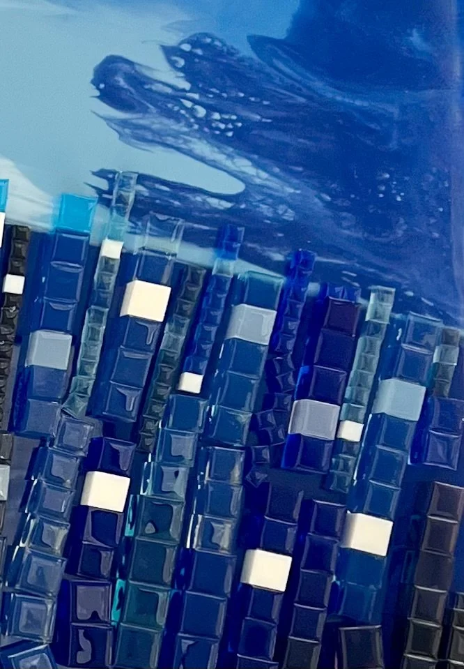 Close-up of a mosaic of small blue, white, and reflective glass tiles with a water reflection at the top.