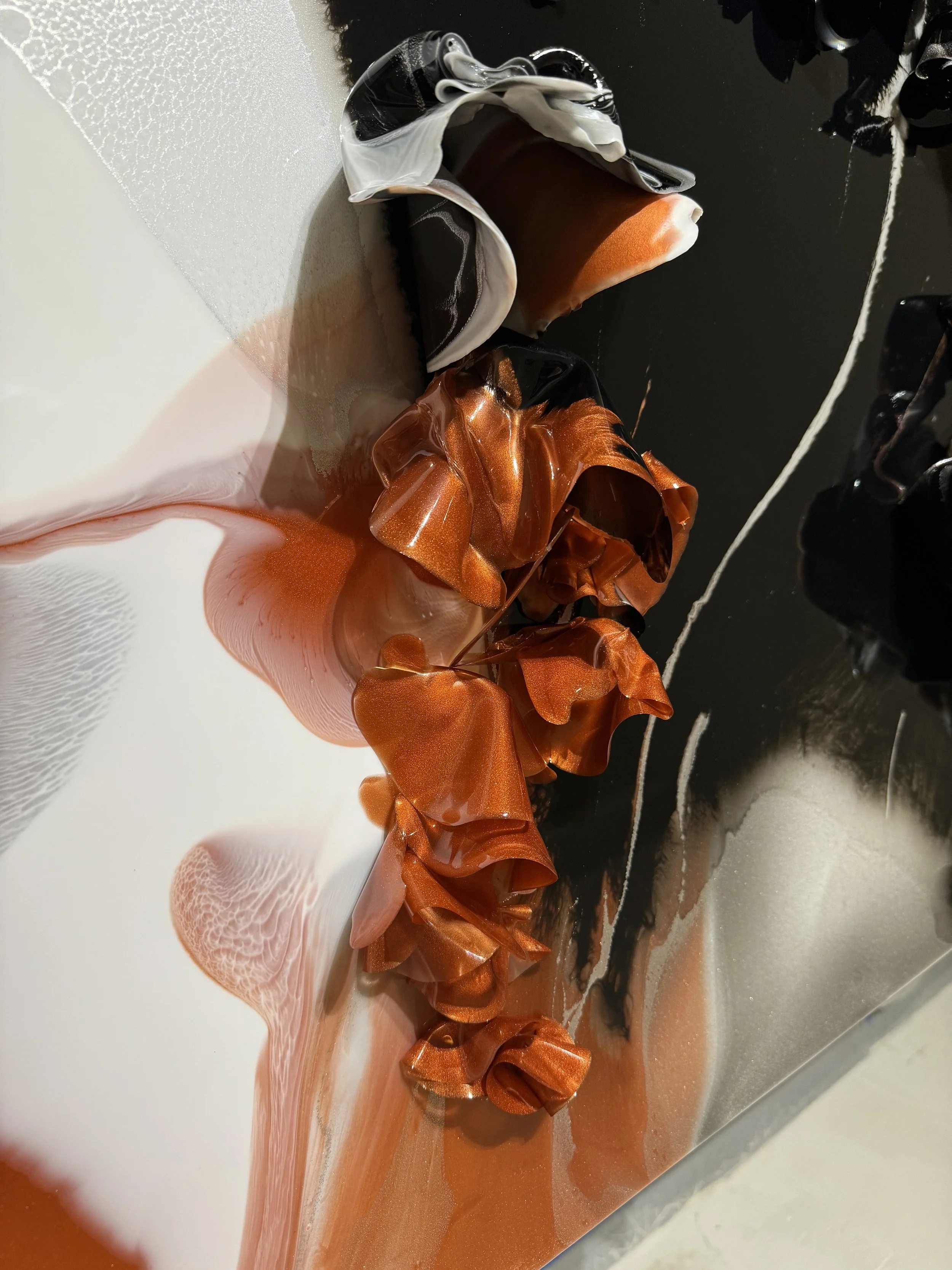 Colorful abstract art scene with flowing orange, black, and white ribbons or fabric, some with metallic sheen, spilling over a surface with reflections.