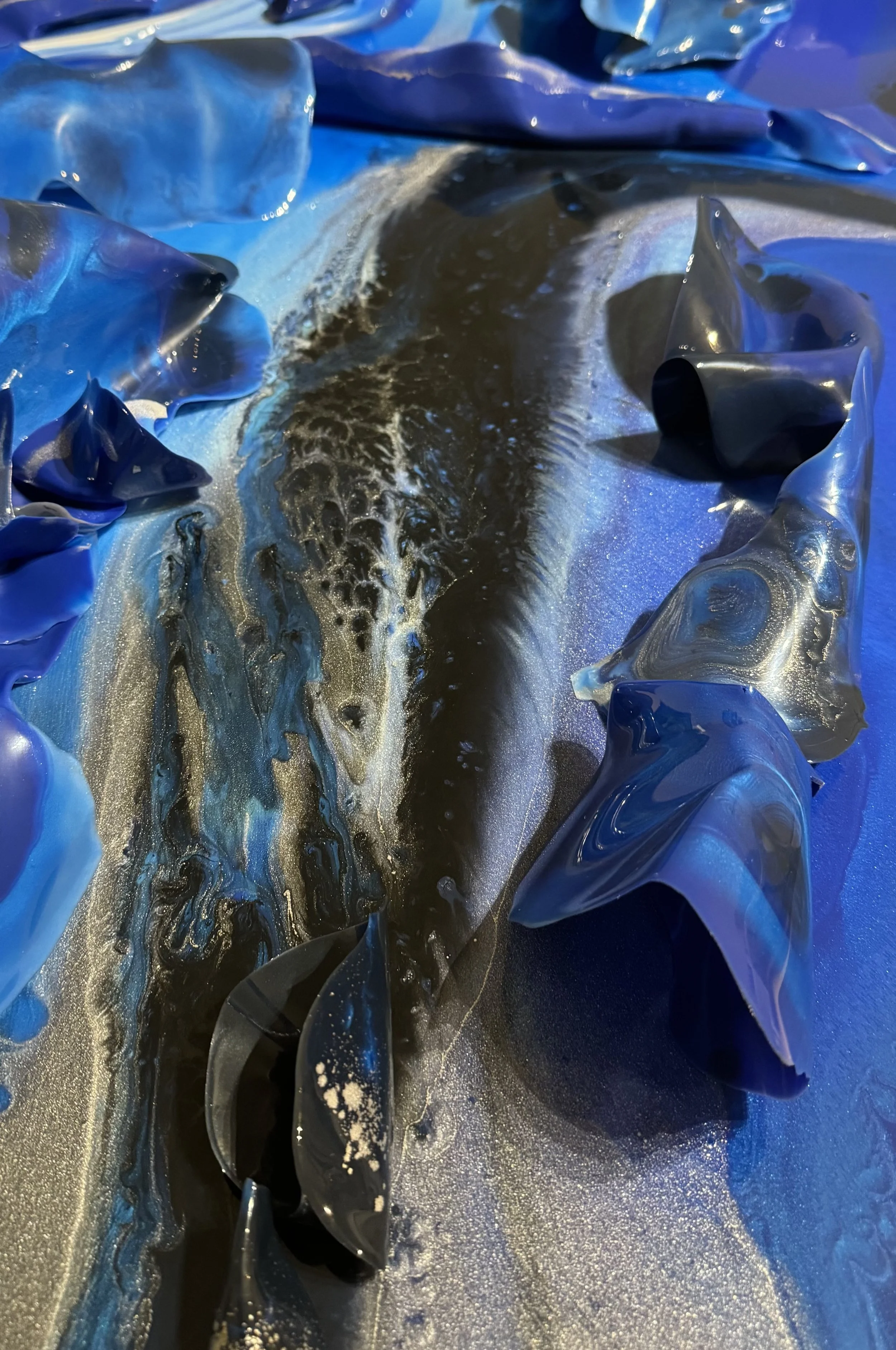 Close-up of an abstract painting with swirling black, gold, and blue colors and layered, crinkled blue material around the edges.