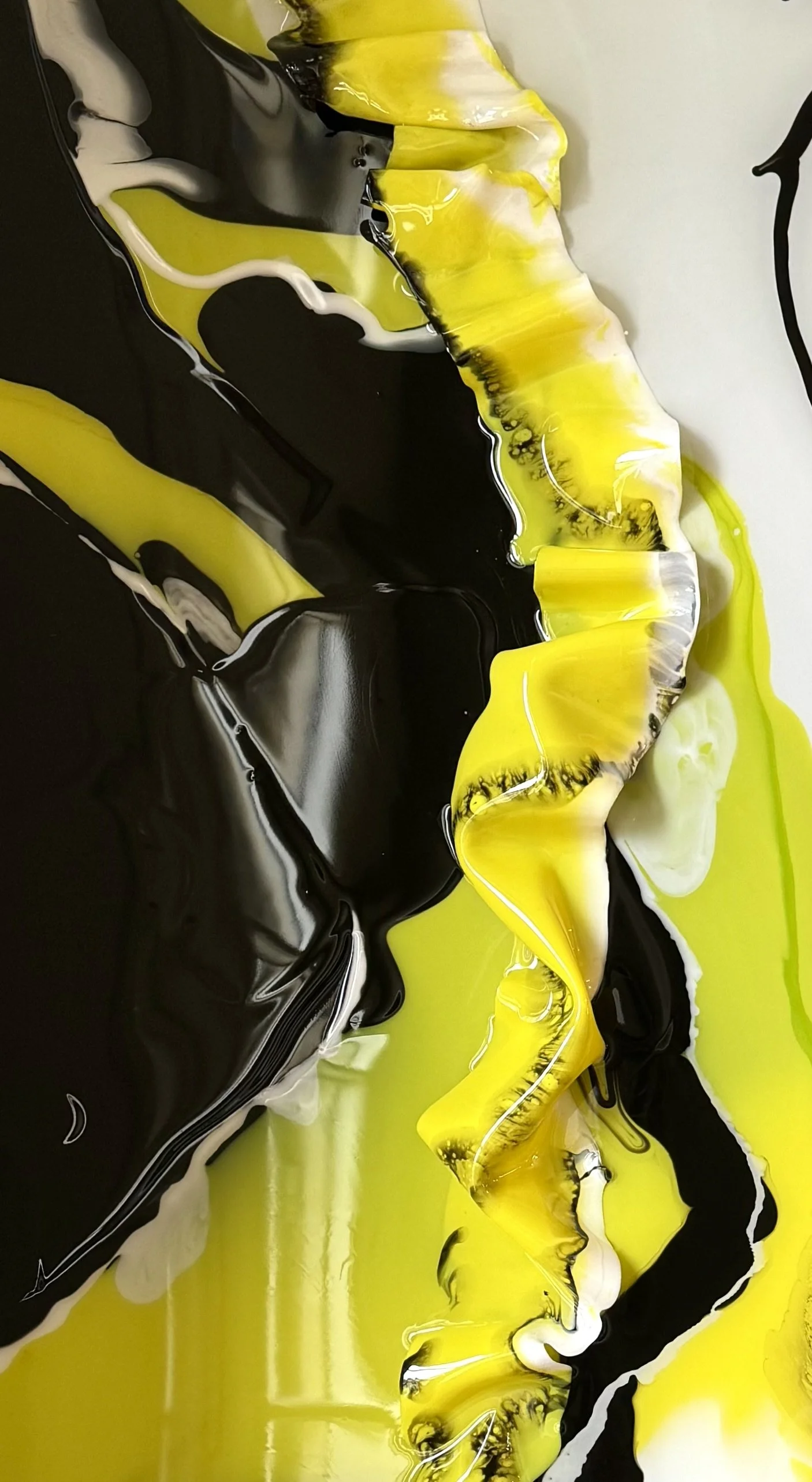 Close-up of abstract fluid art with swirls of black, yellow, white, and hints of green, creating a marbled, flowing pattern.