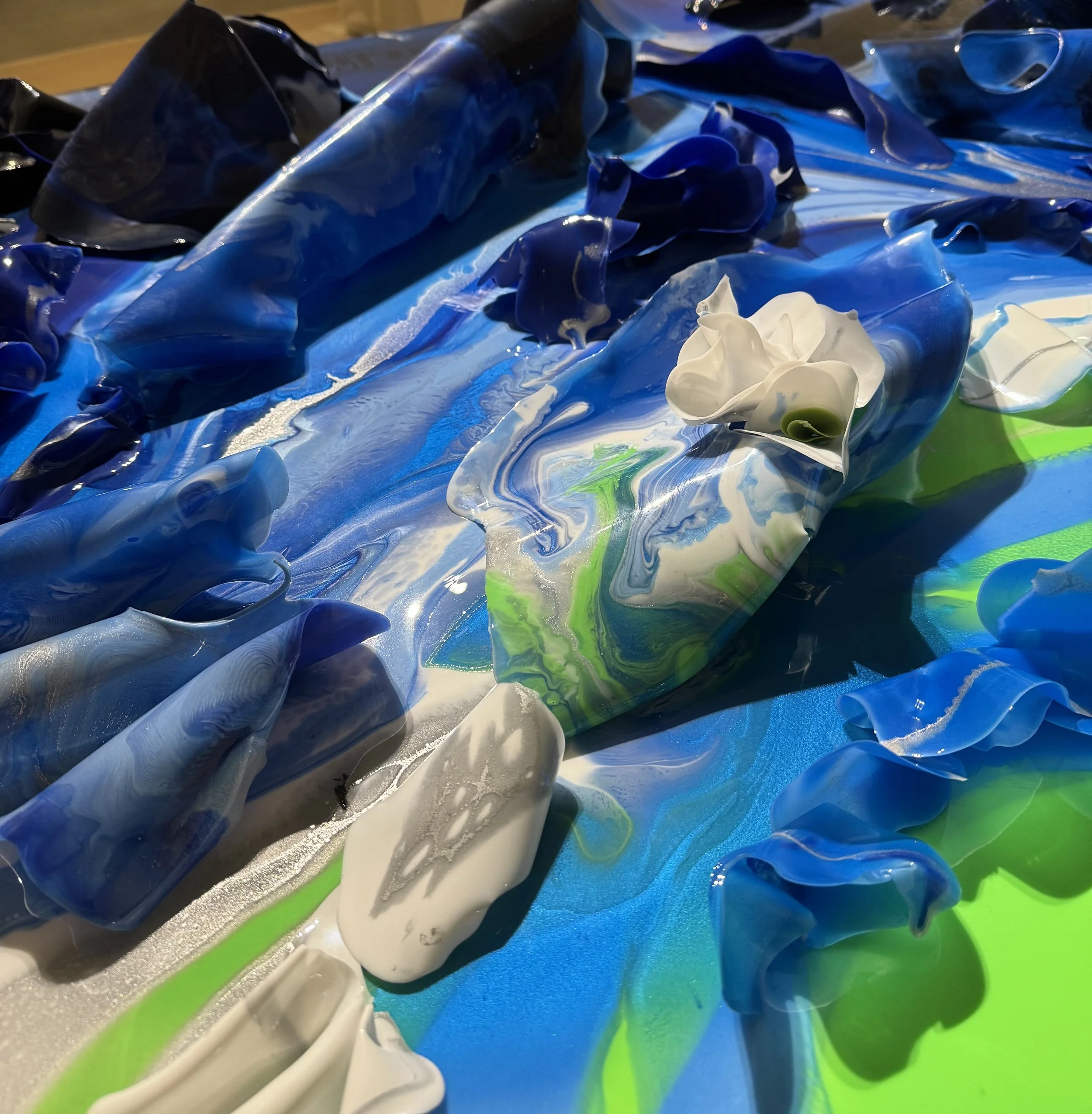 Close-up of abstract, colorful paint swirls in blue, white, and green with some three-dimensional textured areas.